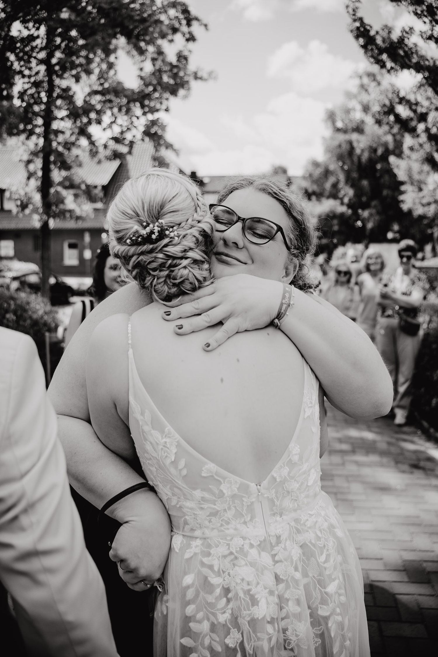 Two people share an emotional embrace at an outdoor wedding celebration in black and white photography.