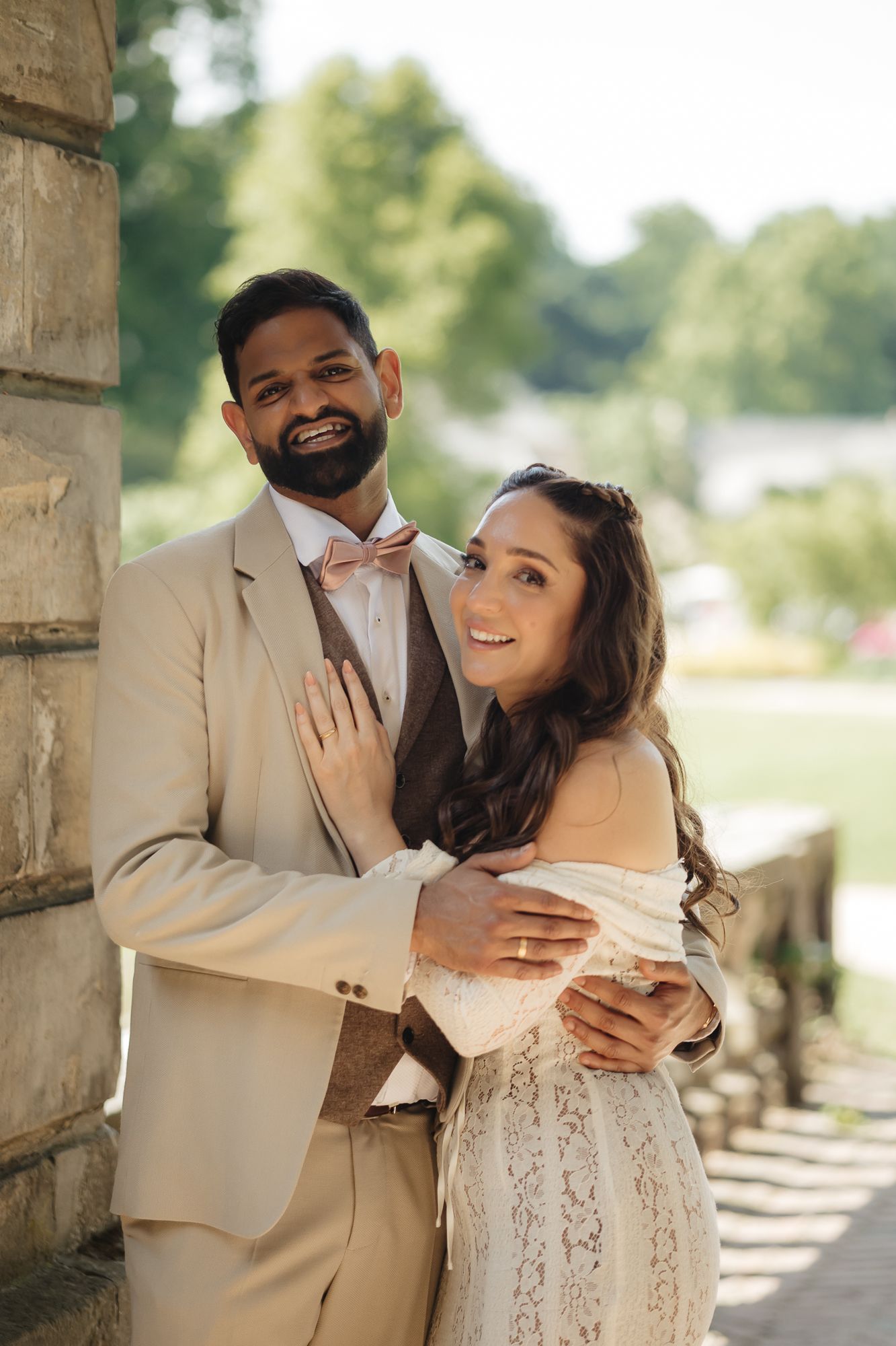 Wedding couple shares intimate moment under stone archway in elegant attire.
