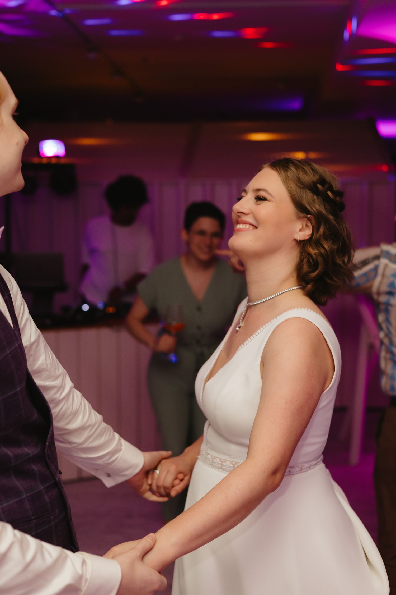 A couple shares a joyful dance moment at their wedding reception under purple and pink lighting.