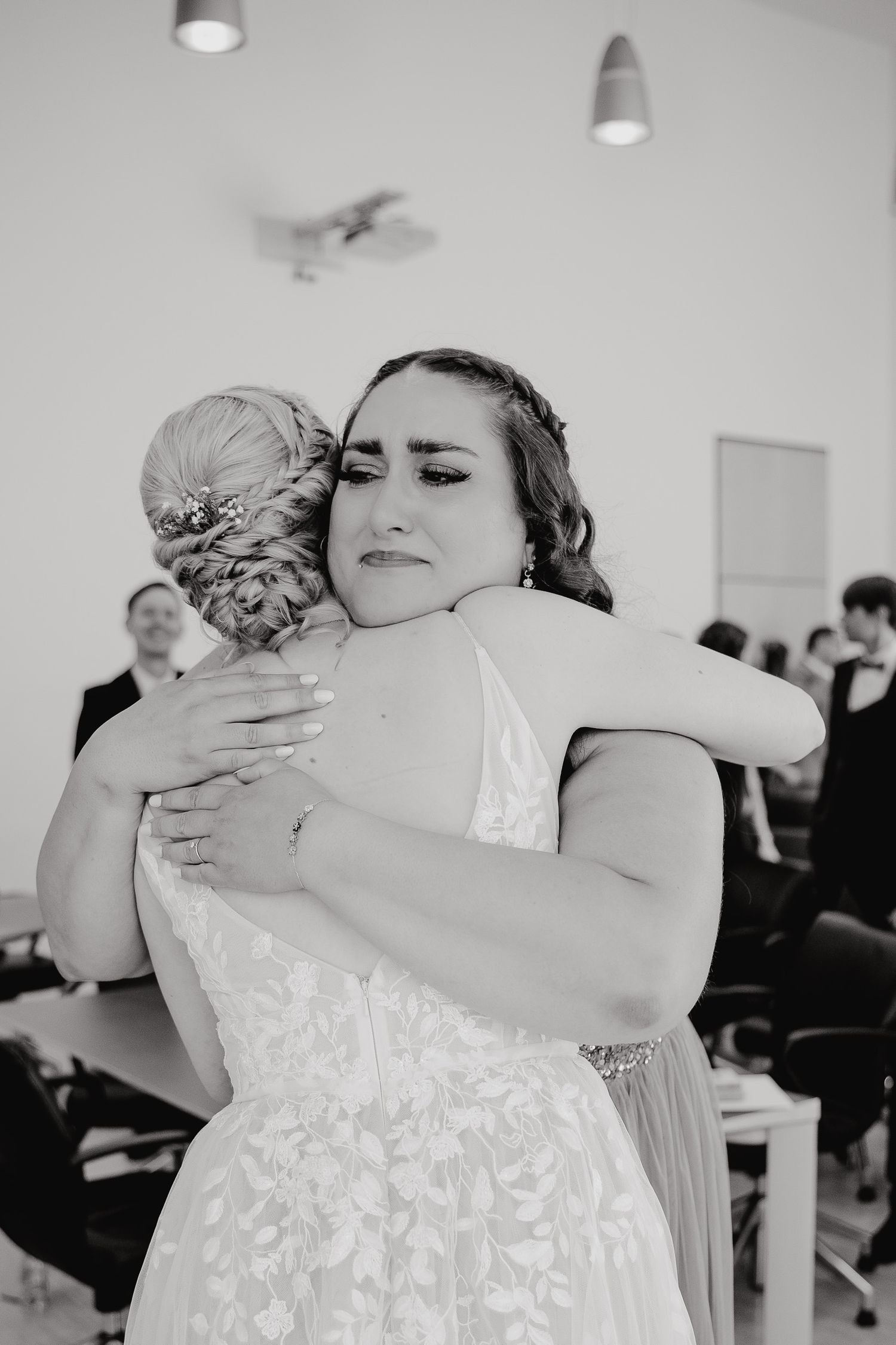Two people share an emotional embrace while wearing formal attire at an indoor event.