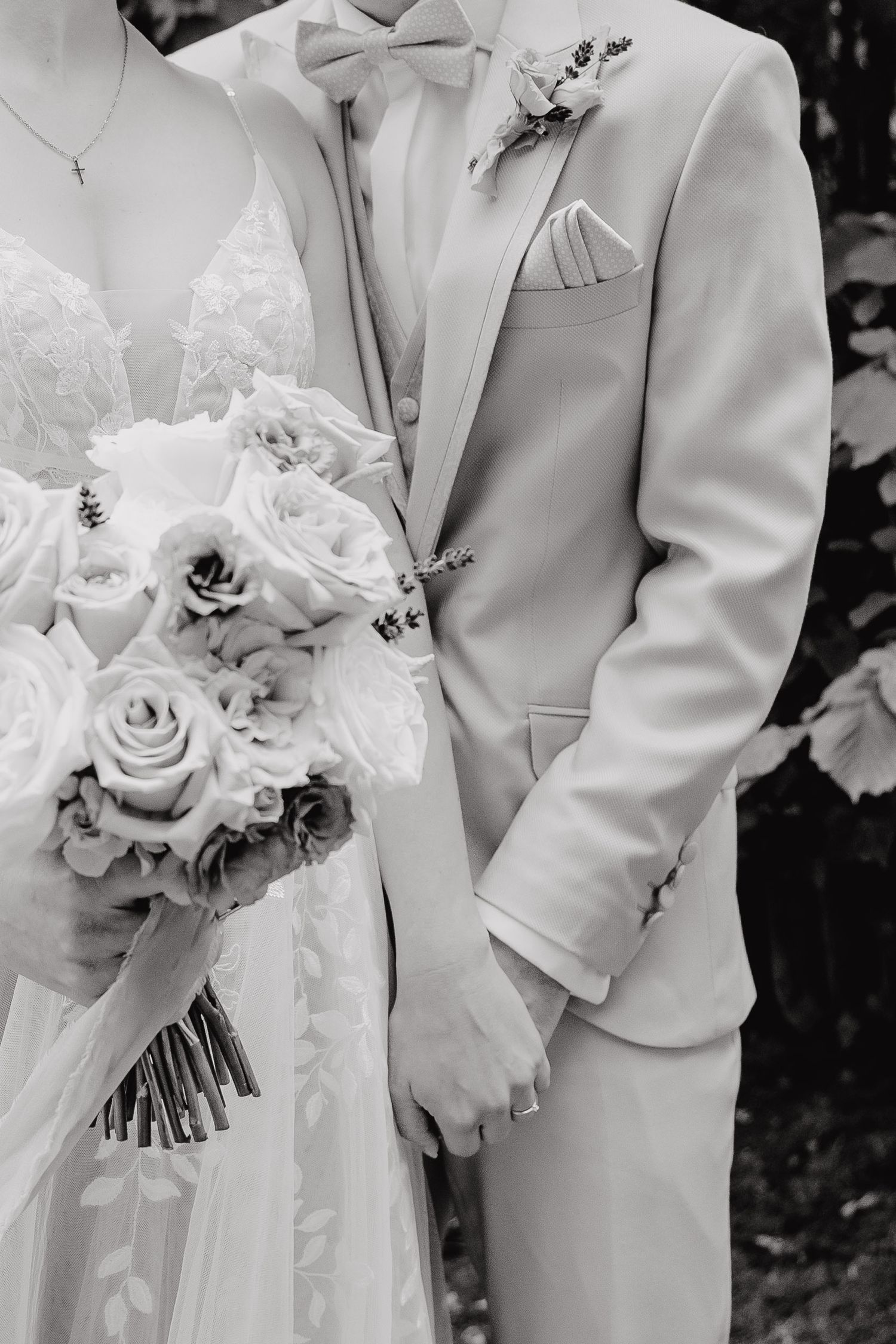 A wedding party in white suits holds elegant white rose bouquets in a black and white photograph.
