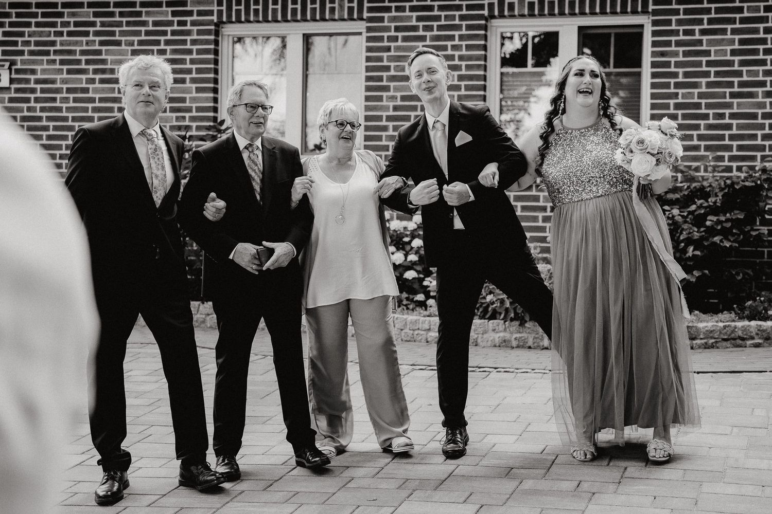 Black and white photo sequence showing wedding party dancing in a line outside a brick building.