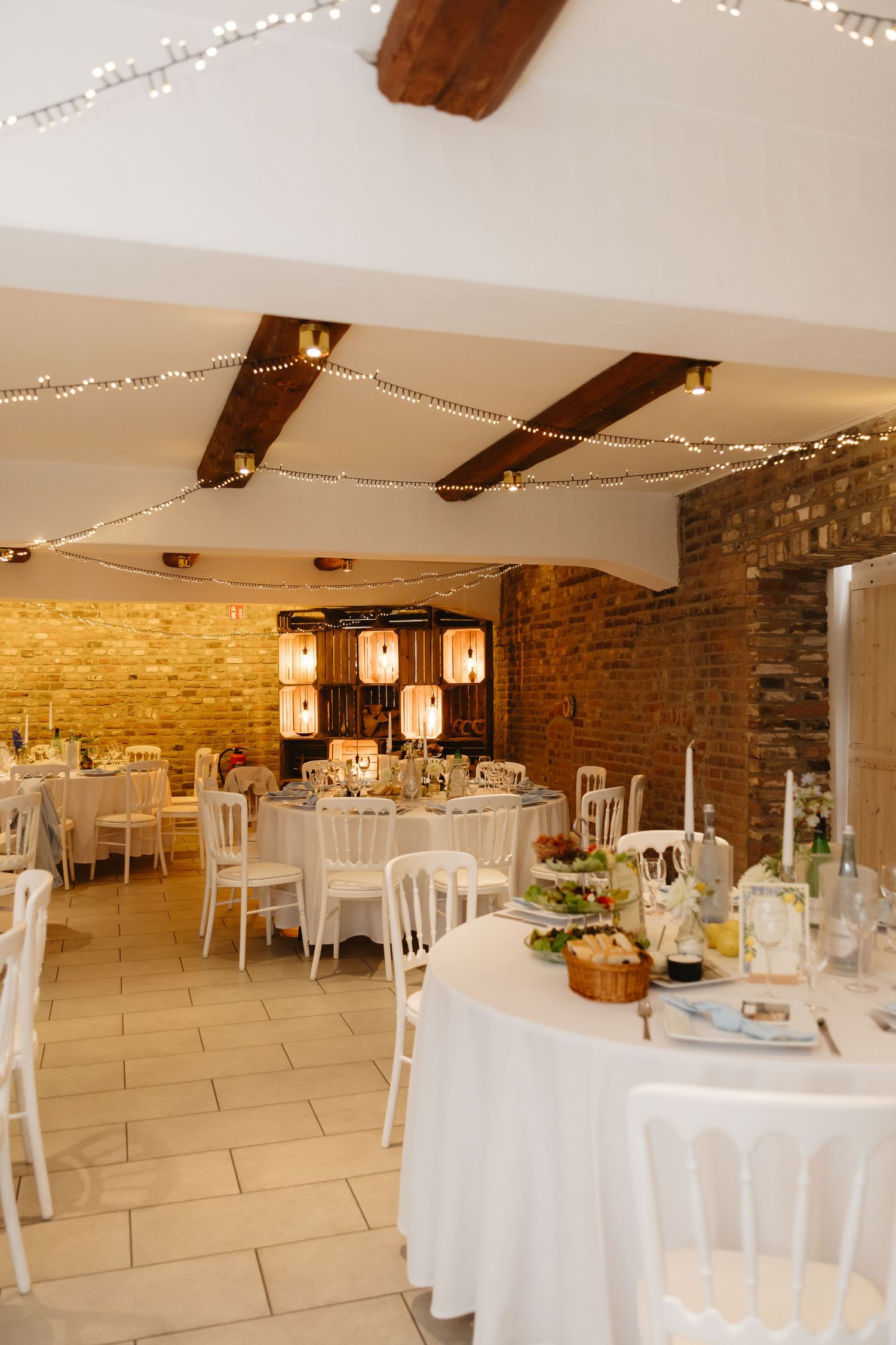 Wedding reception venue with exposed brick walls, string lights, and white table settings.