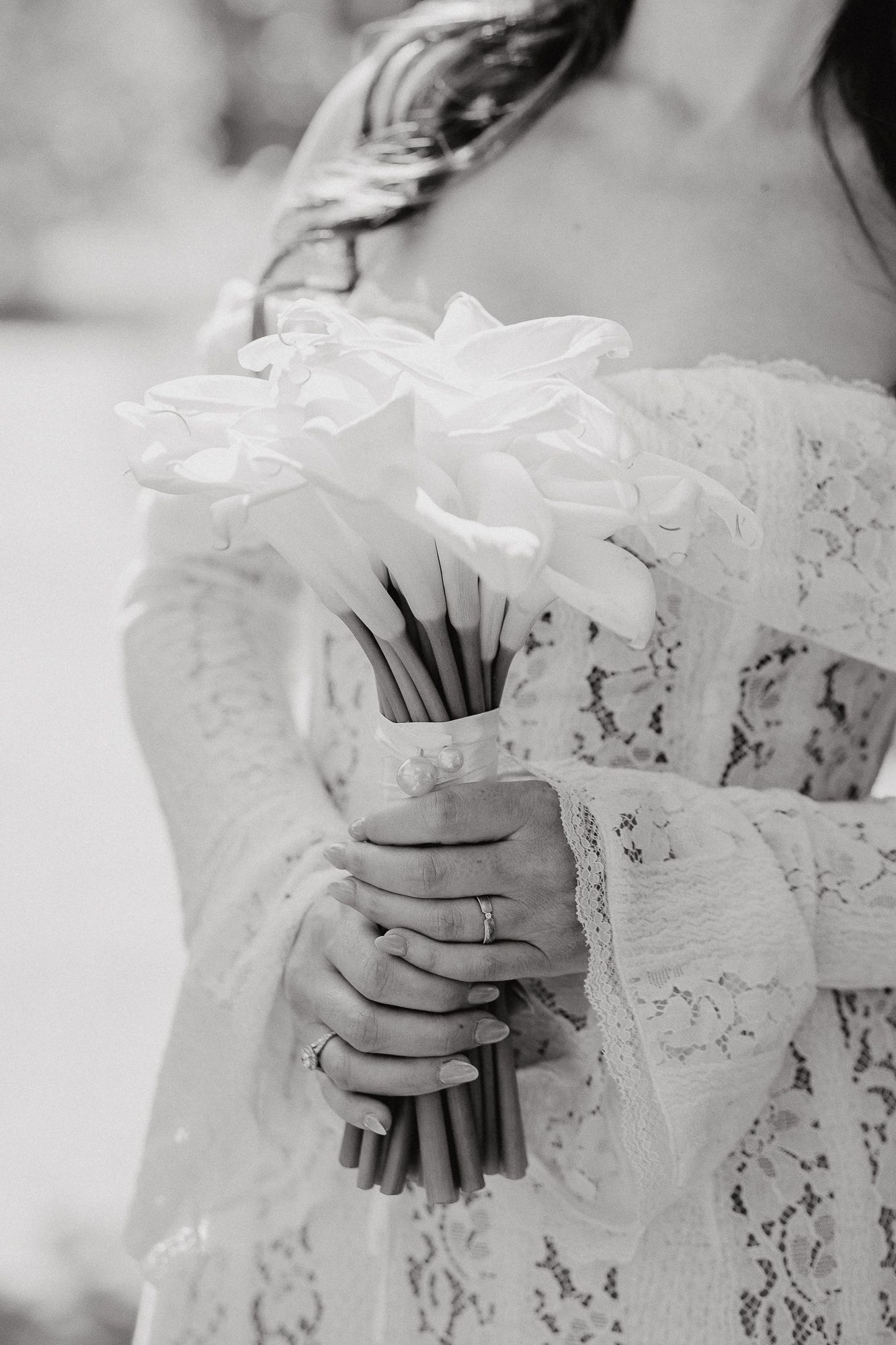 Black and white photo of hands holding a wedding bouquet against lace dress details.