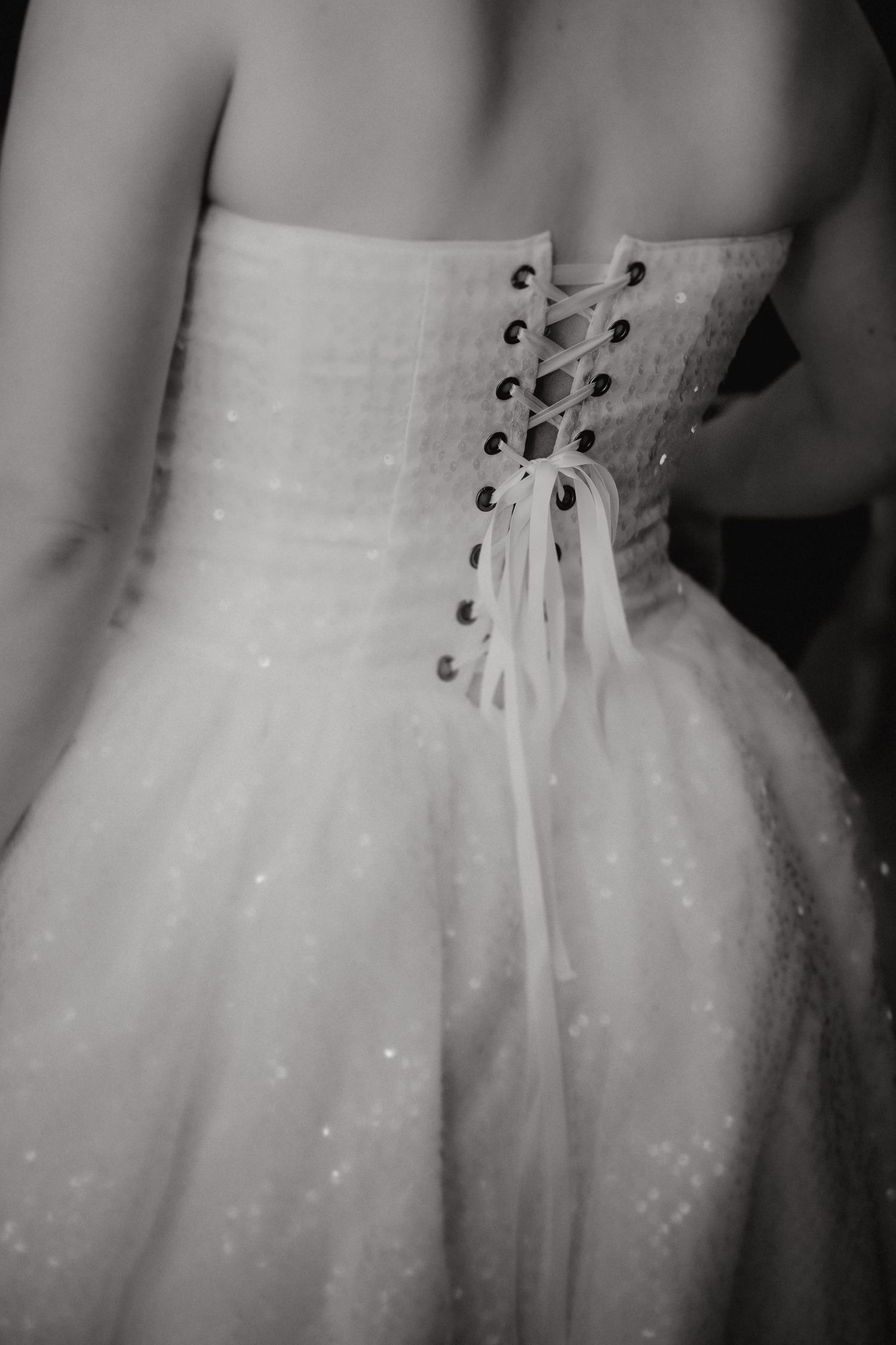Close-up view of a white wedding dress corset back with lace-up ribbon detail and sparkly tulle fabric.