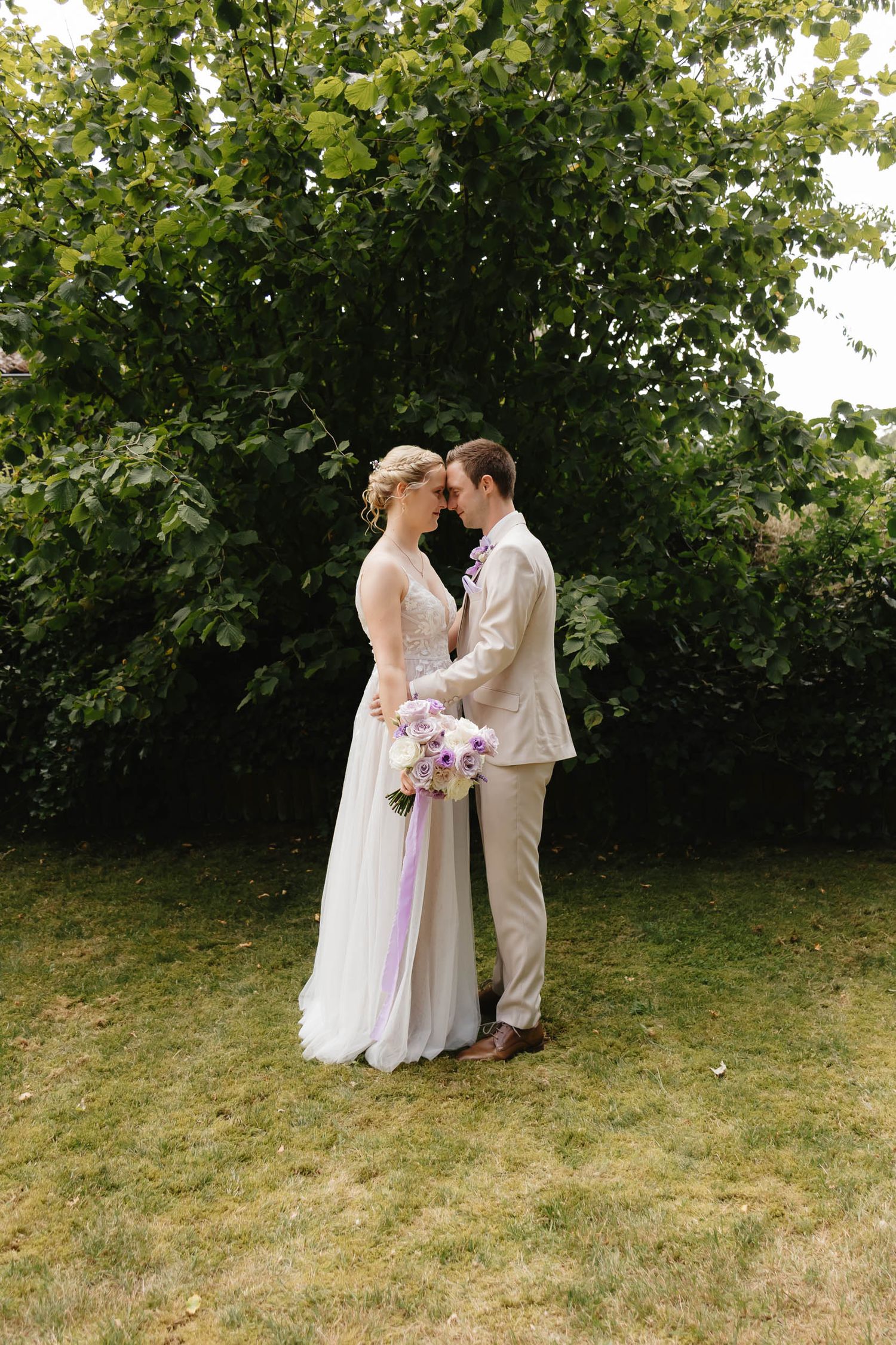 A romantic wedding couple shares intimate moments in a garden setting with green foliage backdrop.