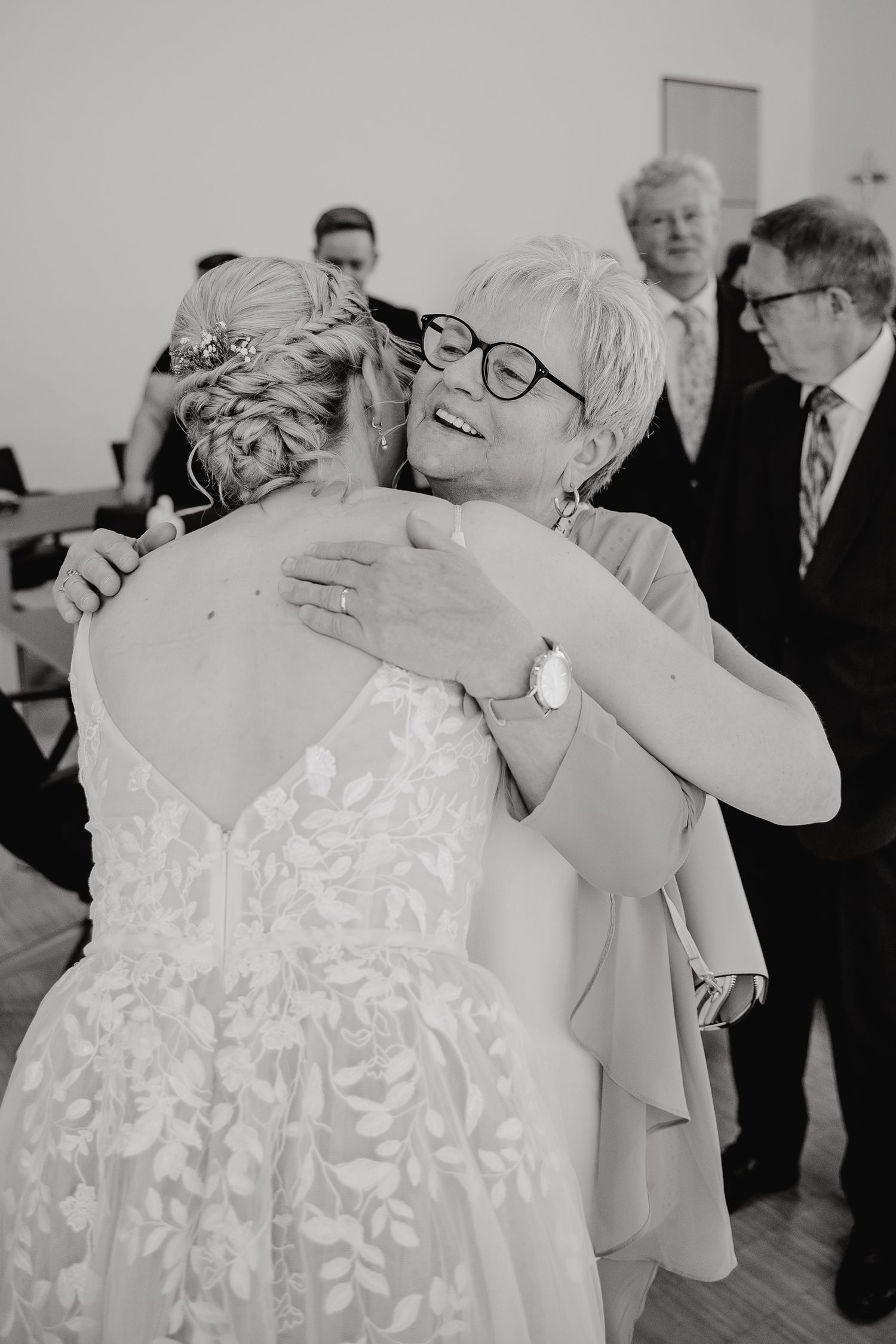 A series of black and white photos showing emotional embraces between people at a wedding celebration.