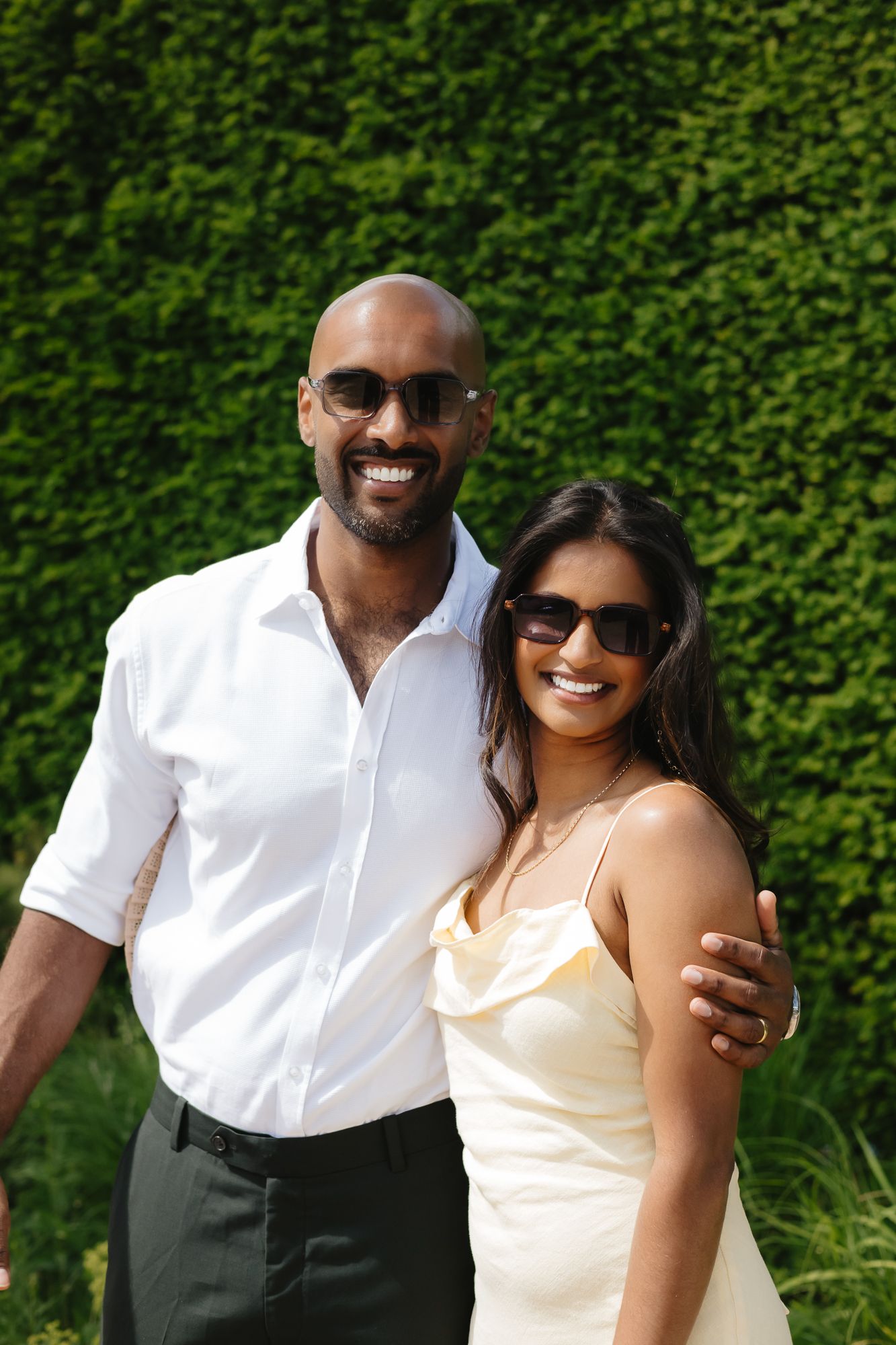 Cheerful outdoor portraits against a lush green hedge background.