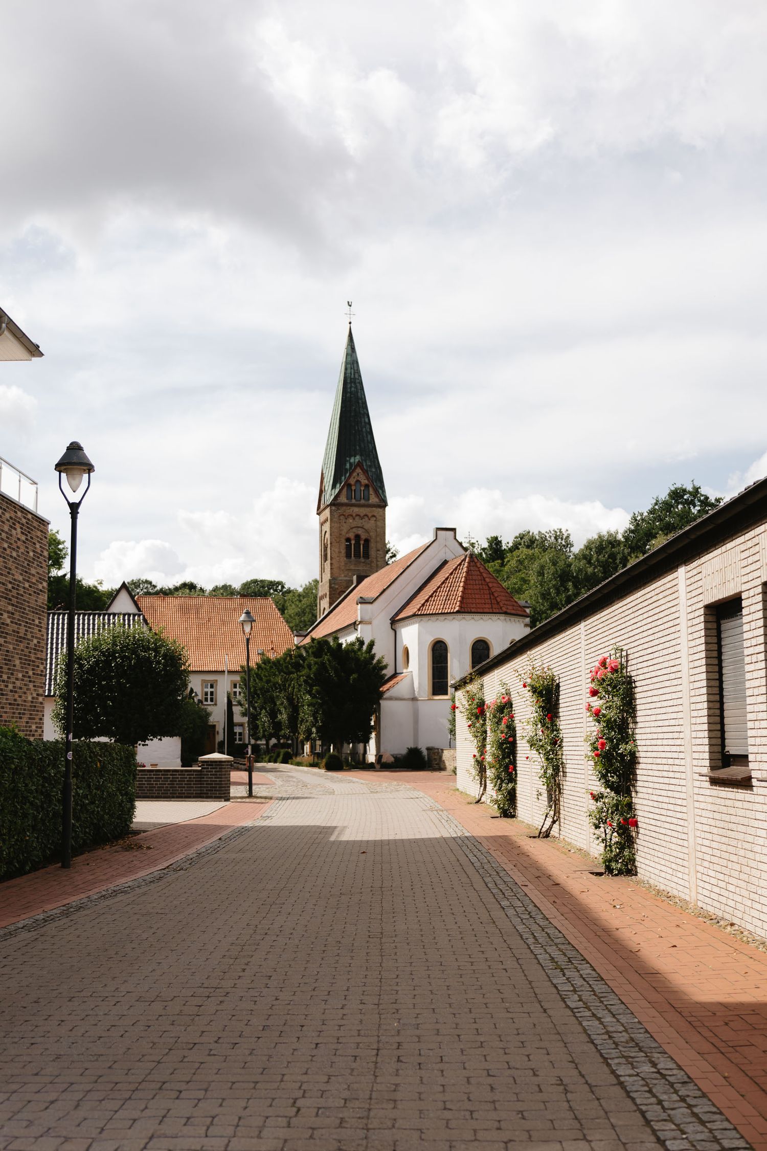 Panoramic view of a charming European village street with white walls, church spire, and cobblestone path.