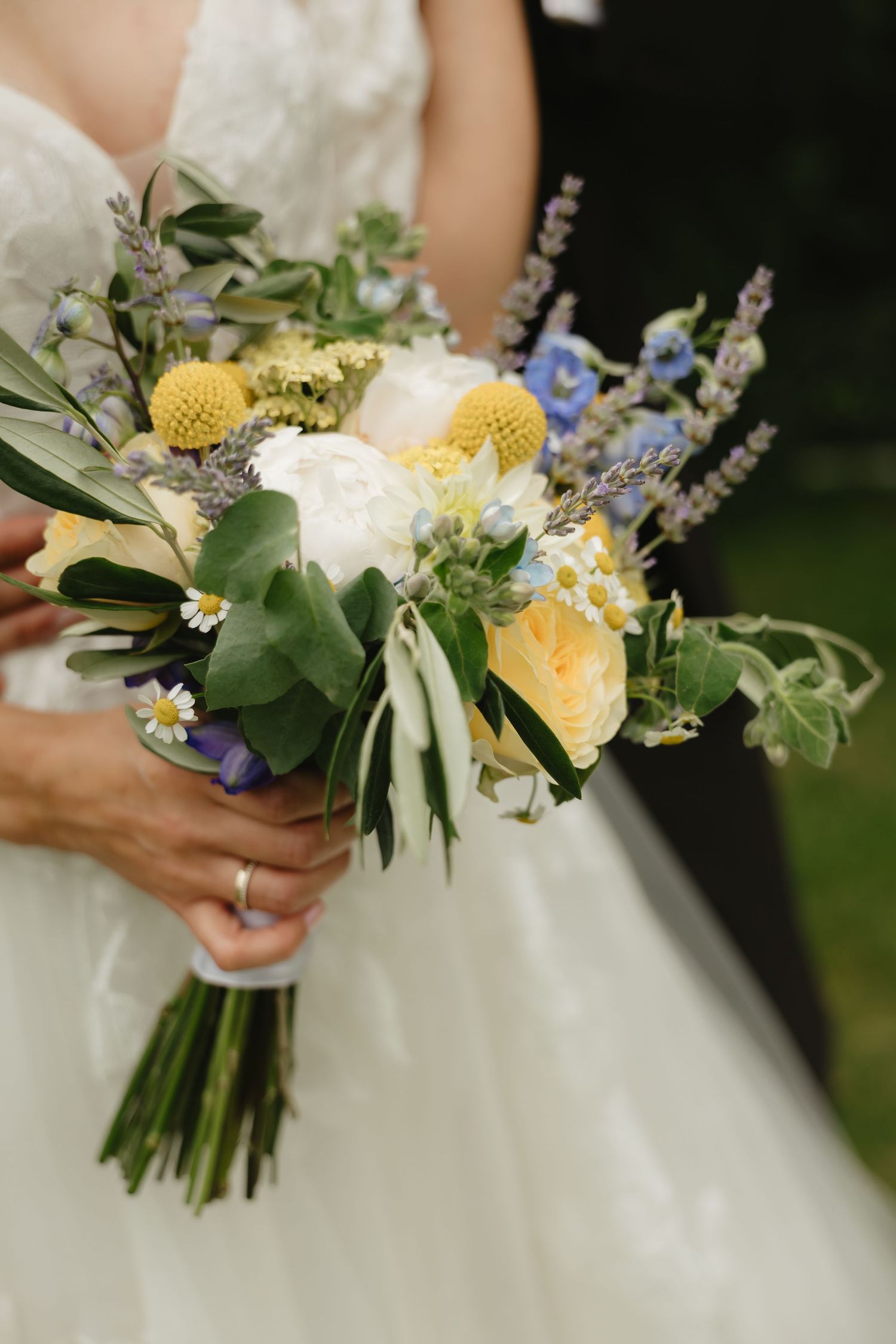 Wedding bouquet with yellow and blue wildflowers, white roses and greenery.