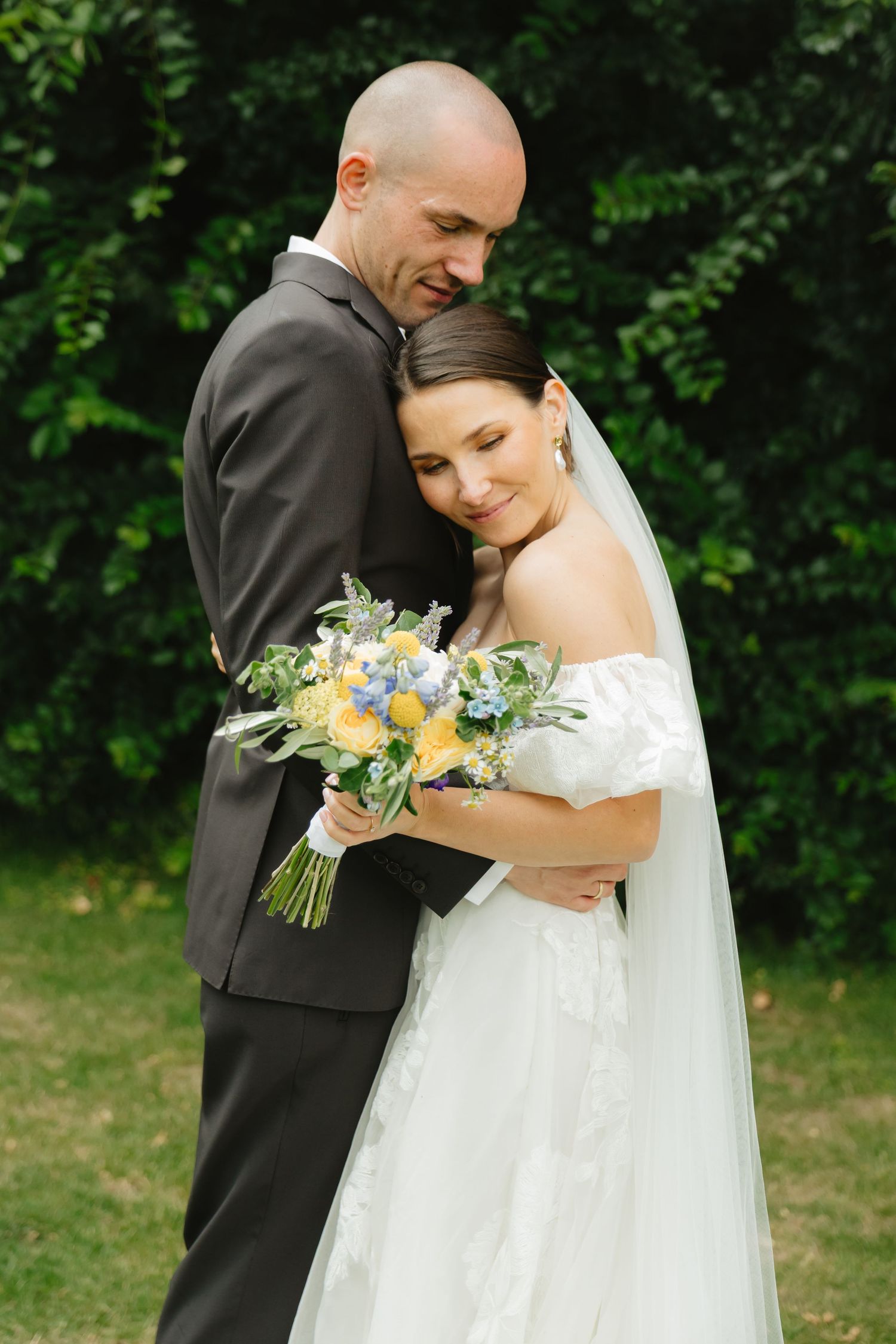 Tender moment between newlyweds with bride holding a blue and yellow bouquet.