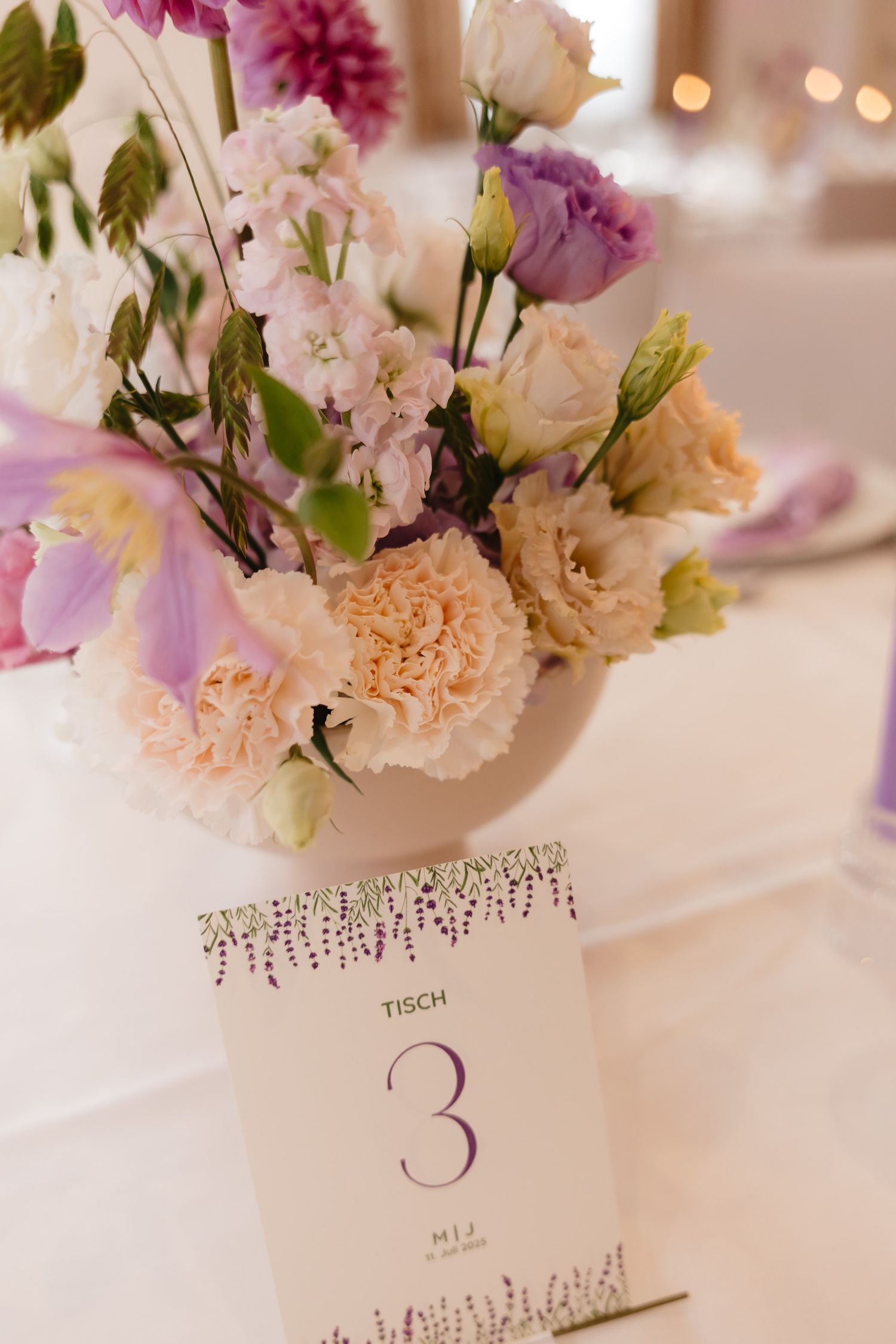 A floral centerpiece with pink and peach carnations next to a table number card decorated with delicate crystal details.
