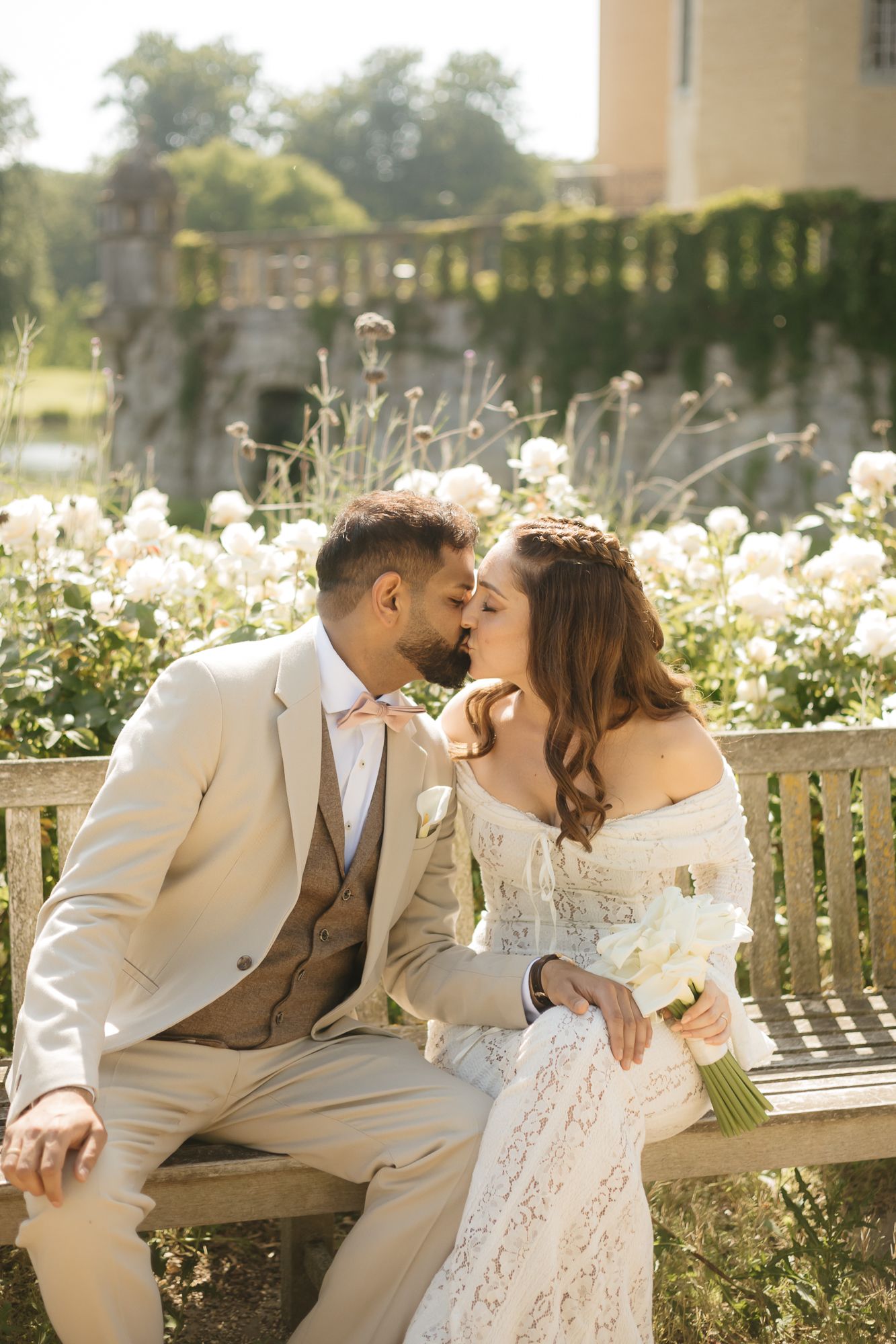 Romantic wedding couple sharing intimate moments on a garden bench surrounded by flowers.