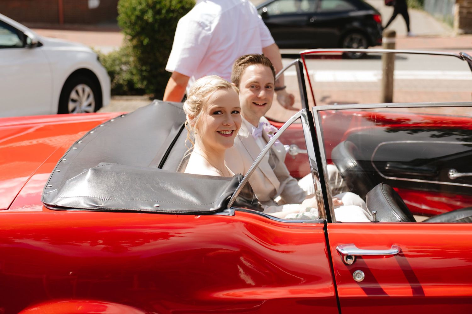 A classic red convertible car parked on a sunny day with occupants enjoying a drive.