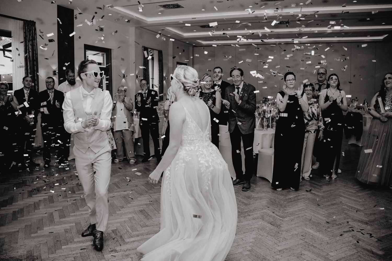 A newlywed couple dances together at their wedding reception while guests surround them on the dance floor.