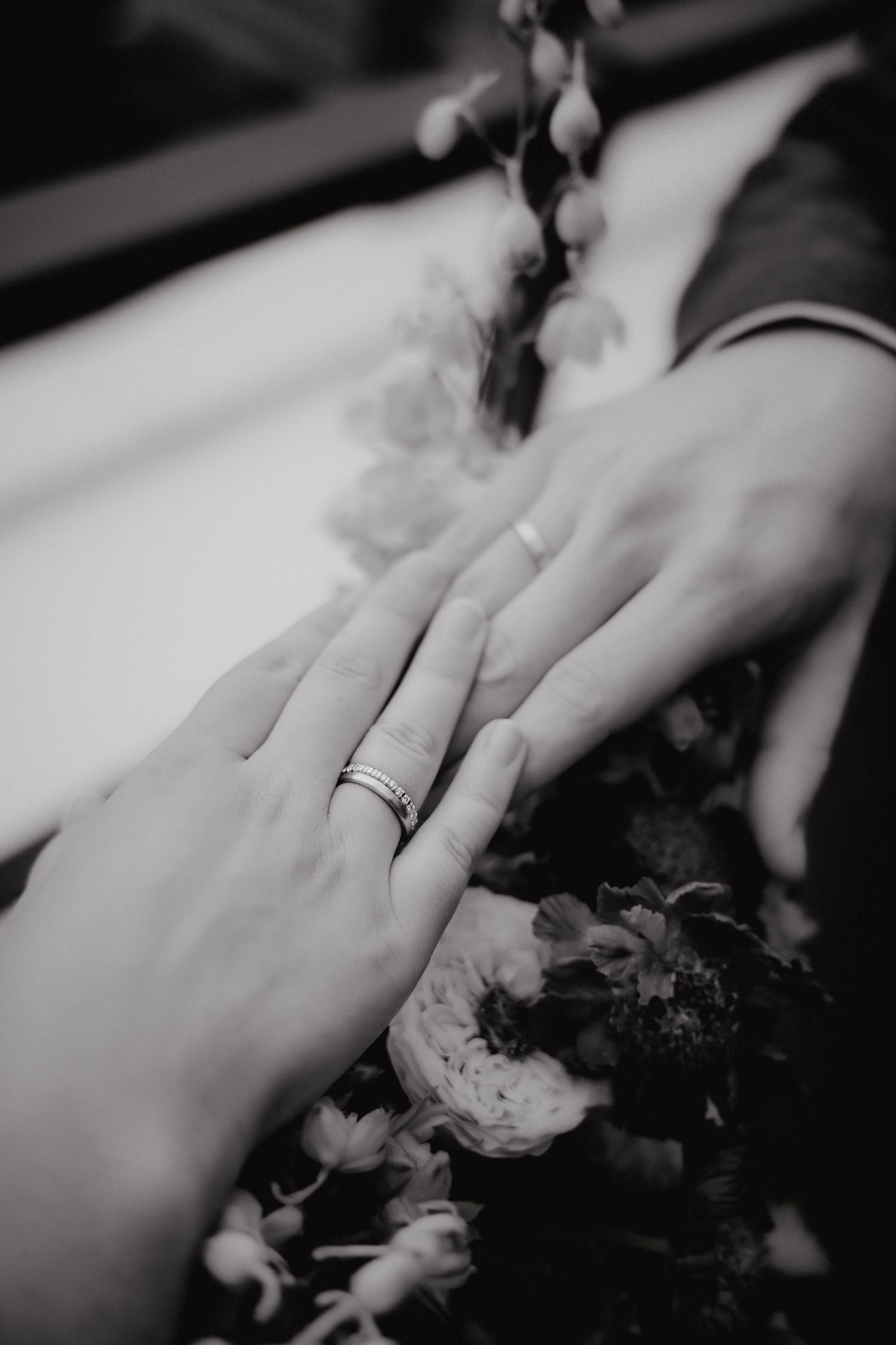 Black and white close-up of hands with wedding ring and delicate floral details in romantic composition.