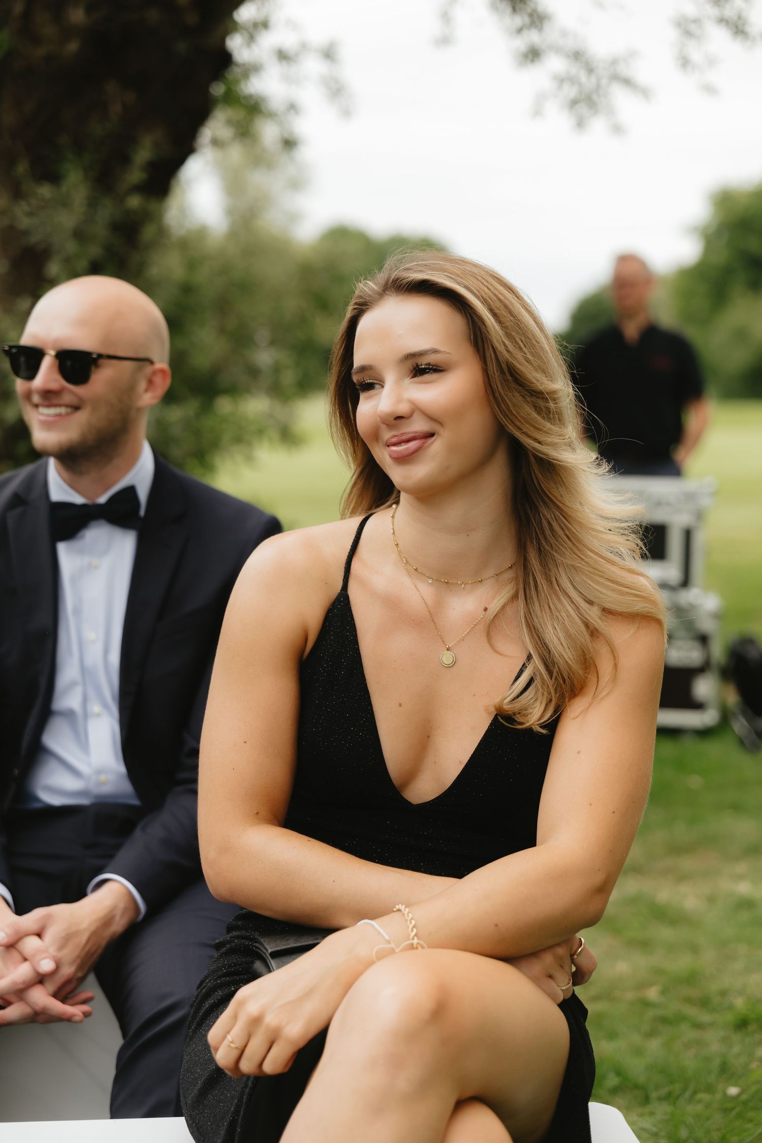 Wedding guests in formal attire sitting and smiling outdoors.