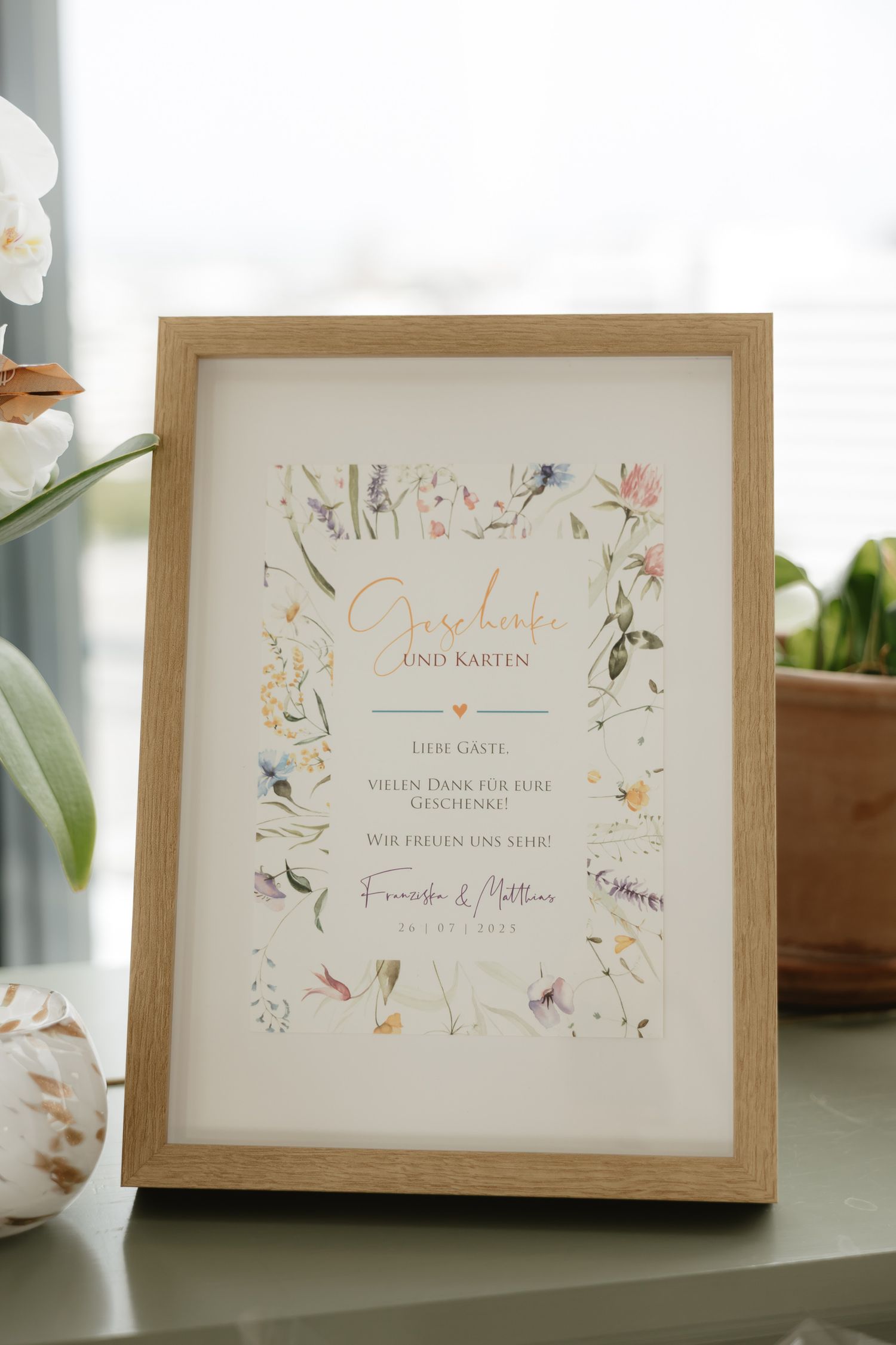 Elegant framed wedding invitation card with delicate floral design and calligraphy text displayed in wooden frame.