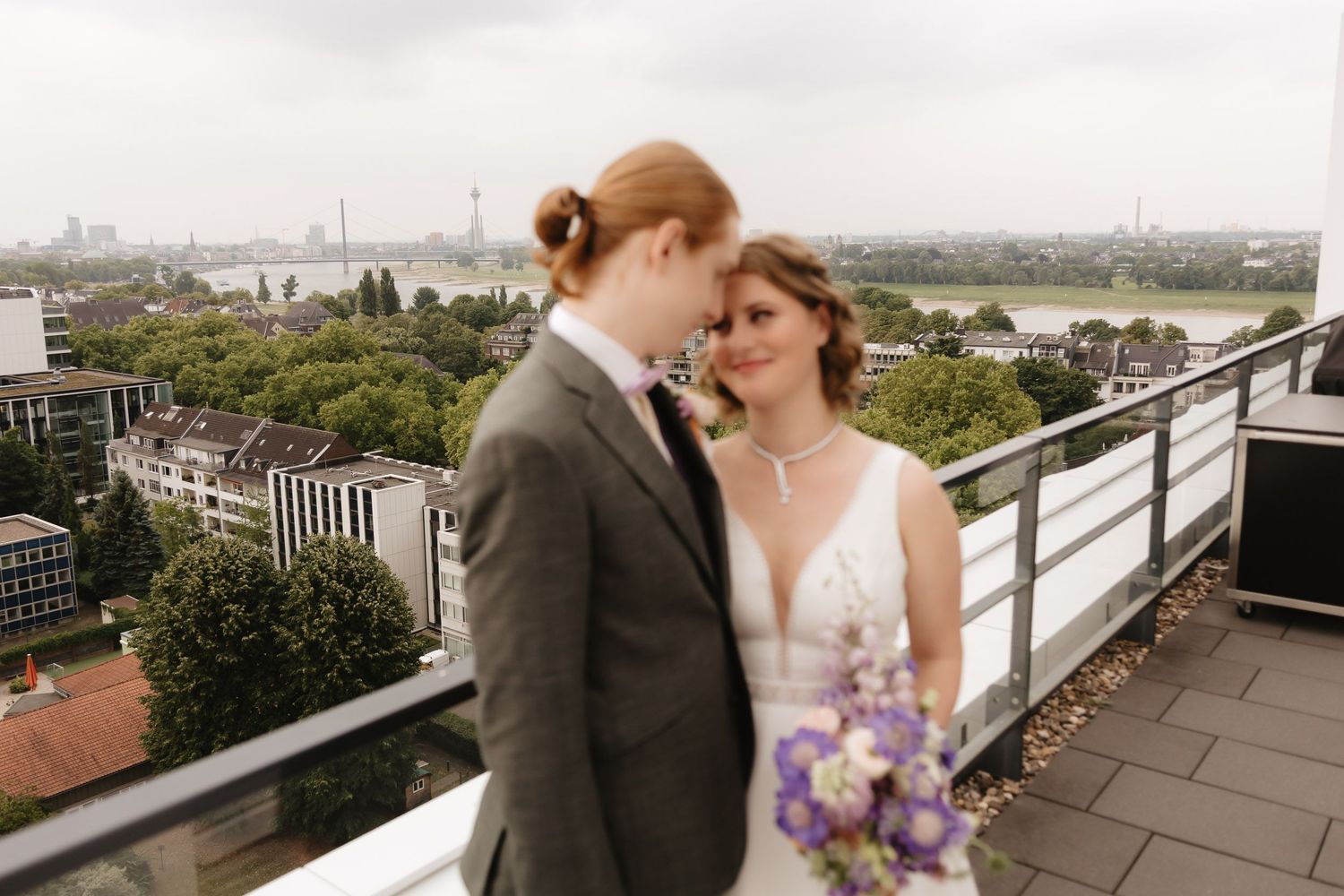 A romantic rooftop moment overlooking a cityscape with purple flowers and elegant wedding attire.