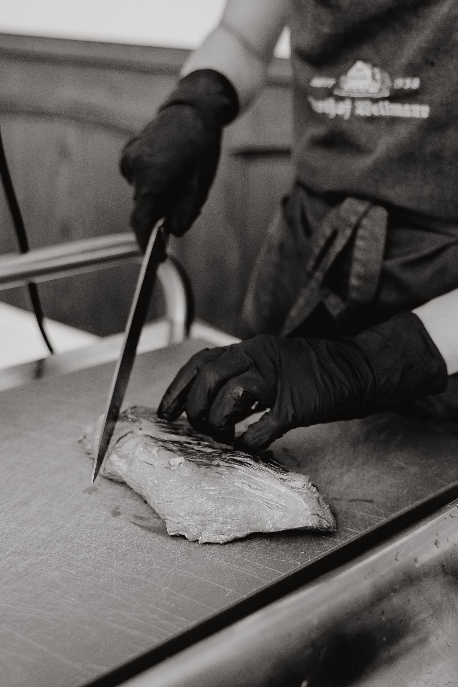 Black and white close-up sequence showing hands slicing meat on a cutting board with a sharp knife.