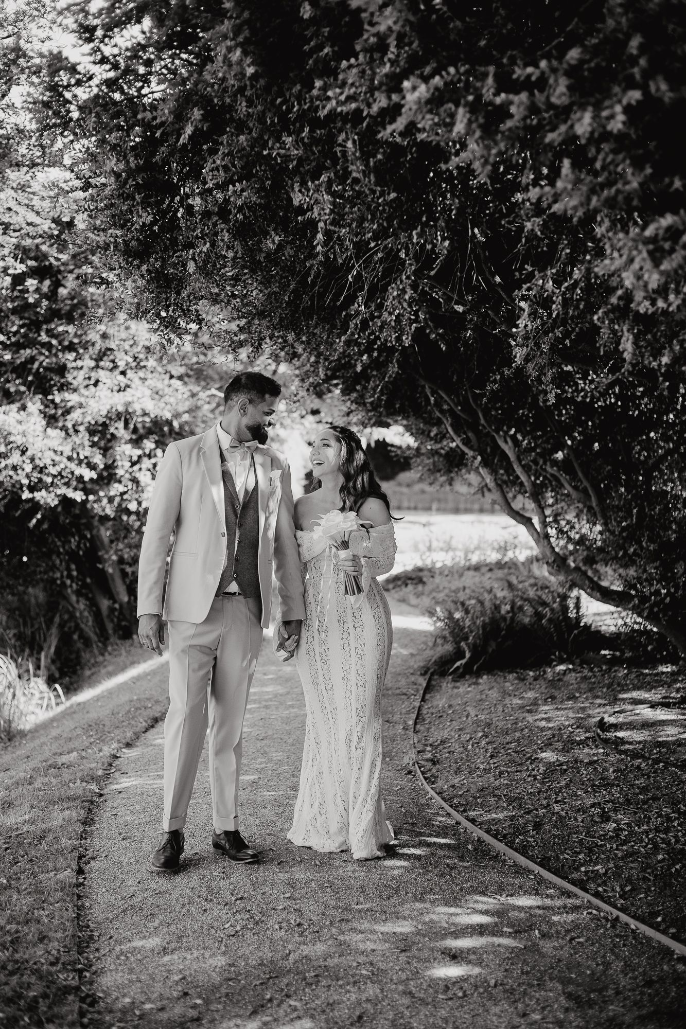 Black and white wedding photo of couples walking through a tree-lined path.
