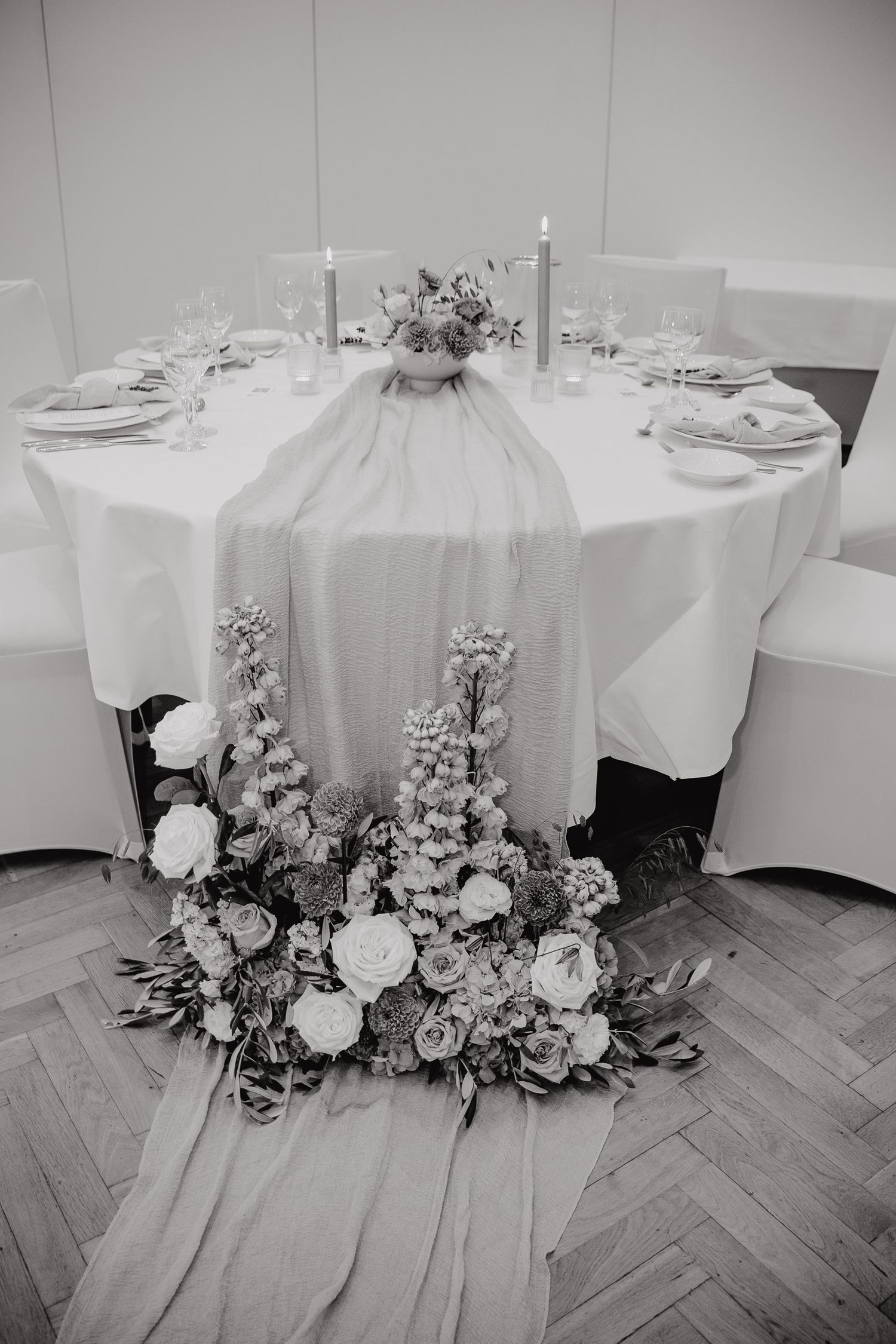 Round banquet tables with white tablecloths and elegant floral centerpieces arranged in a reception hall setting.