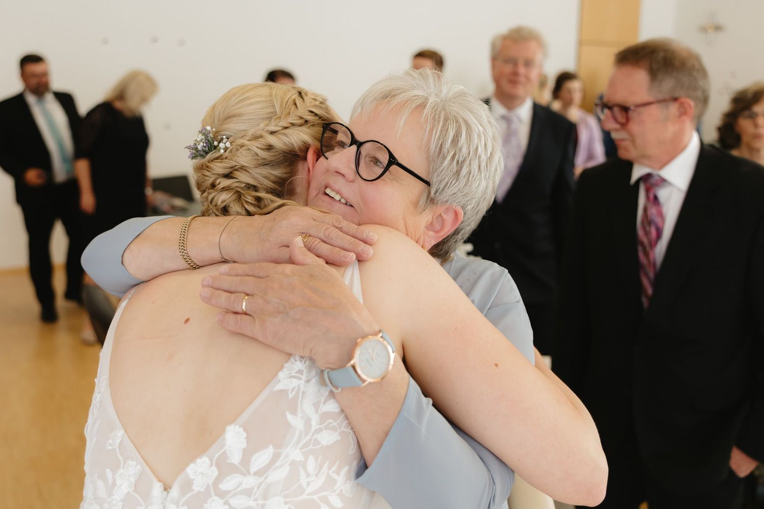 A couple shares an emotional embrace during a wedding ceremony as guests look on in the background.
