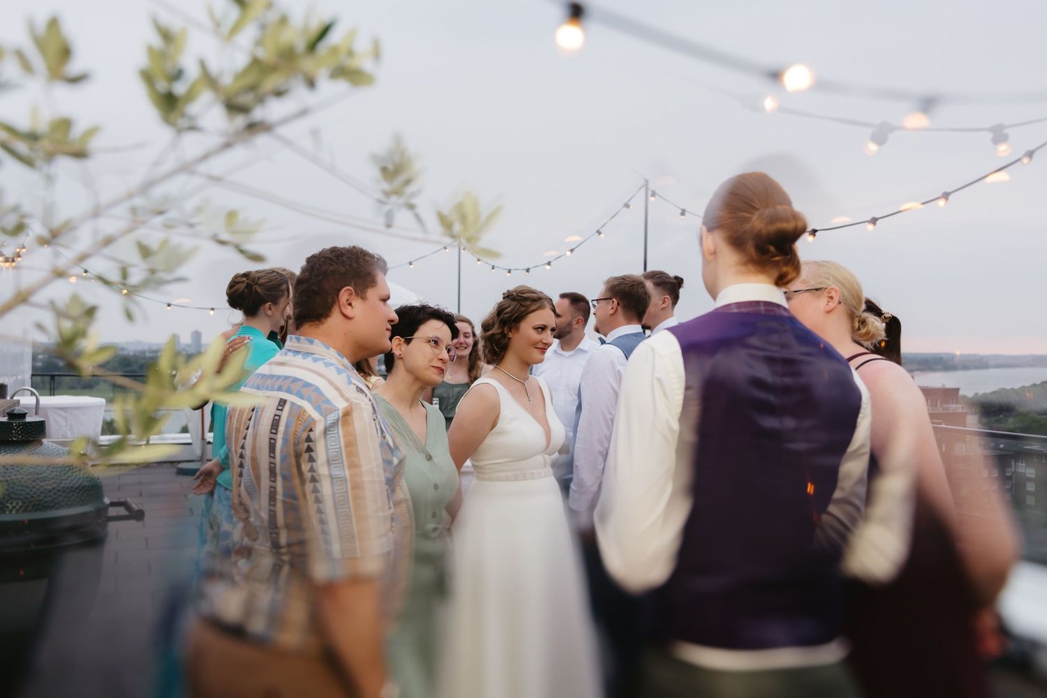 Wedding guests gather on an outdoor deck at dusk with string lights glowing overhead and palm trees in the background.