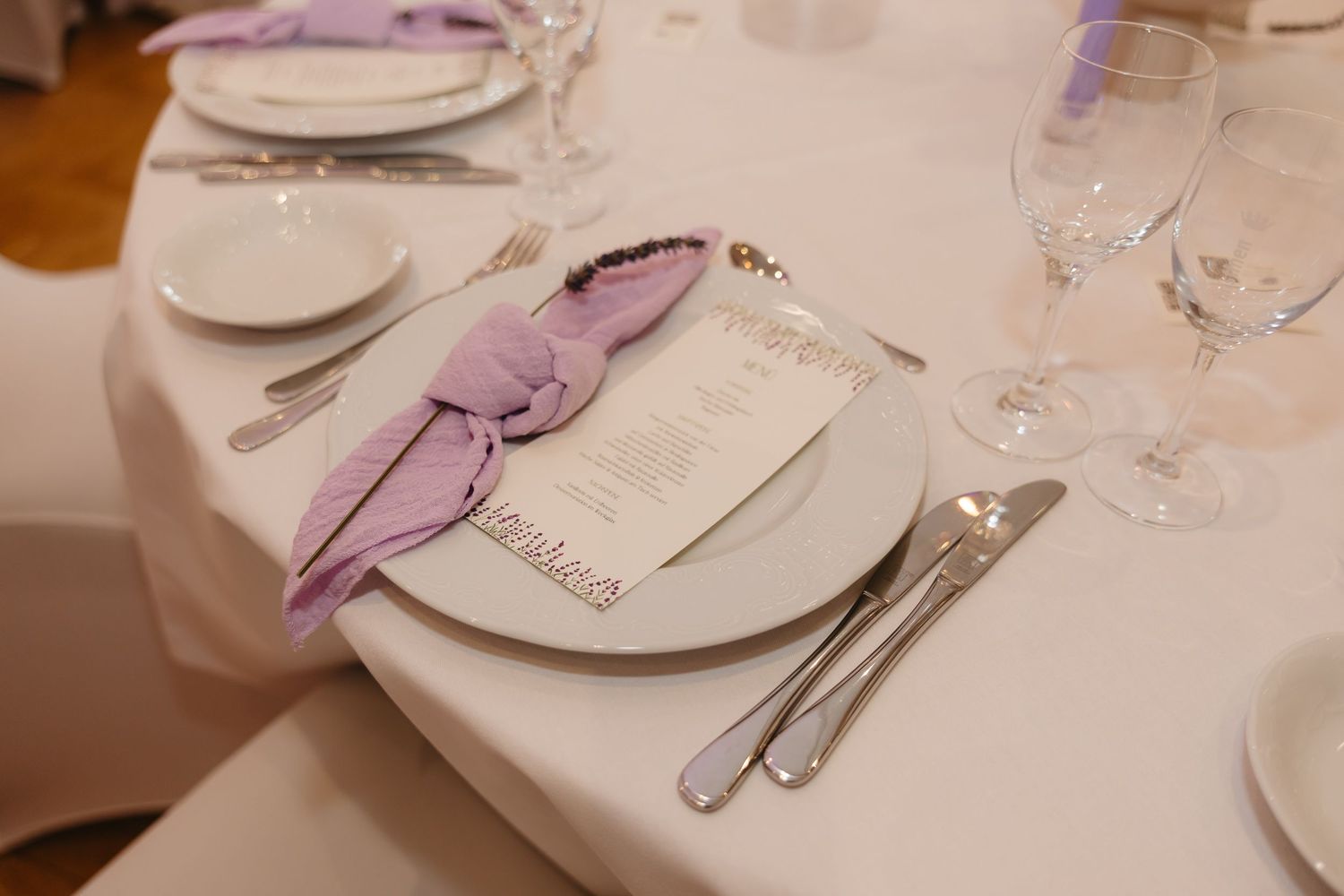 Elegant place settings at a formal dinner with purple napkins and white plates on a cream tablecloth.