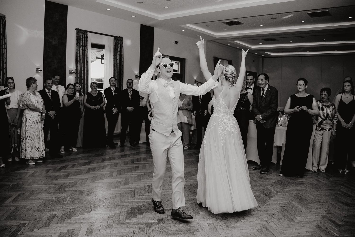 Couples dancing together at a wedding reception in a ballroom with wooden floors and elegant lighting.