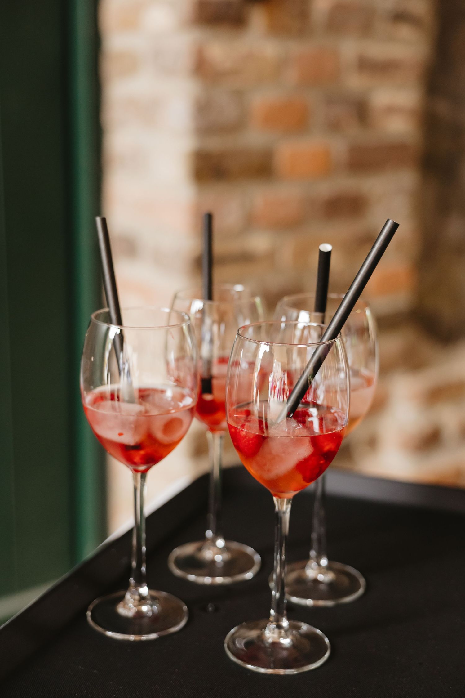 Red cocktails in stemmed glasses arranged on a dark surface with brick wall background.