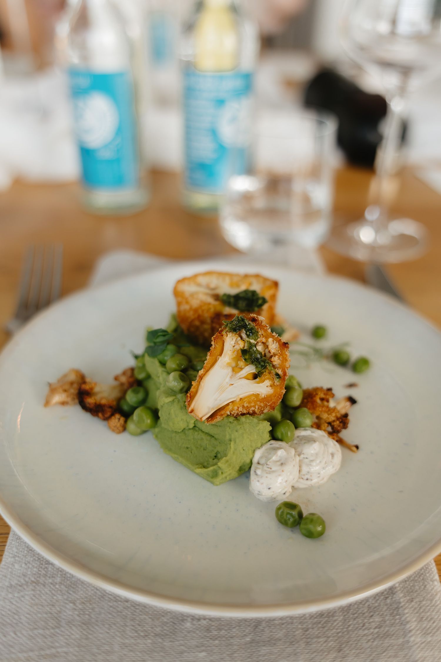 Elegant plated dish featuring crispy fish with avocado puree, fresh peas and herbs on a white ceramic plate.