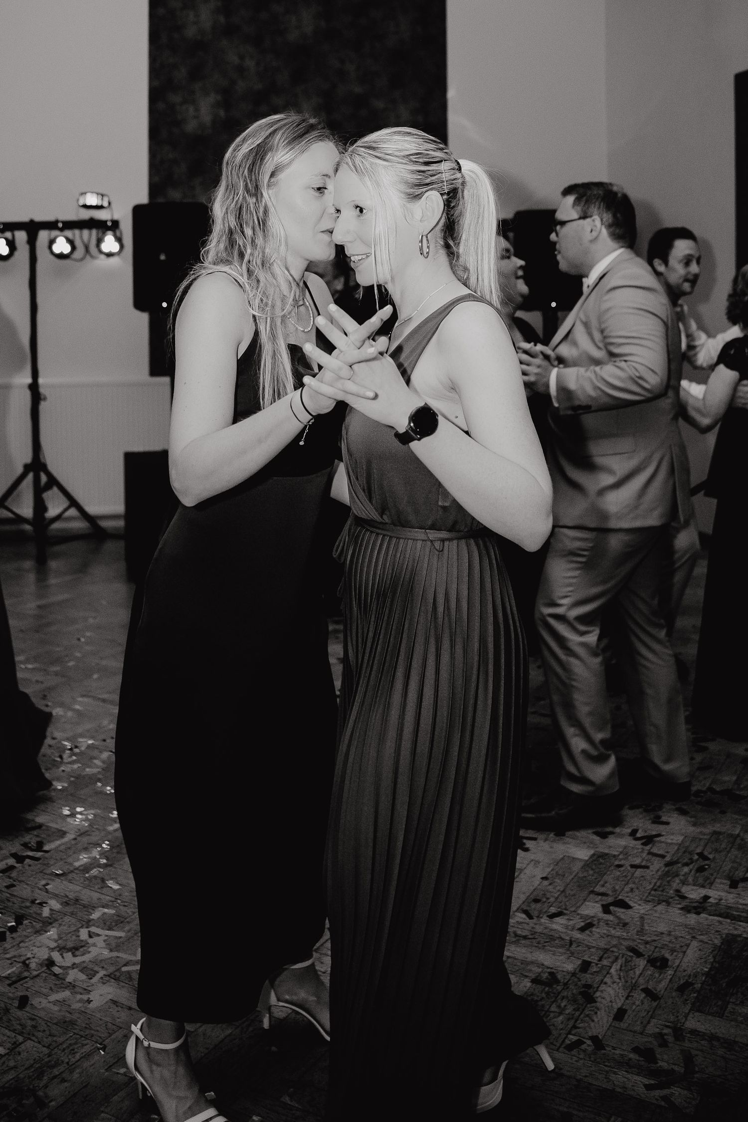 Couples dancing together at a dimly lit reception venue with confetti scattered on the floor.