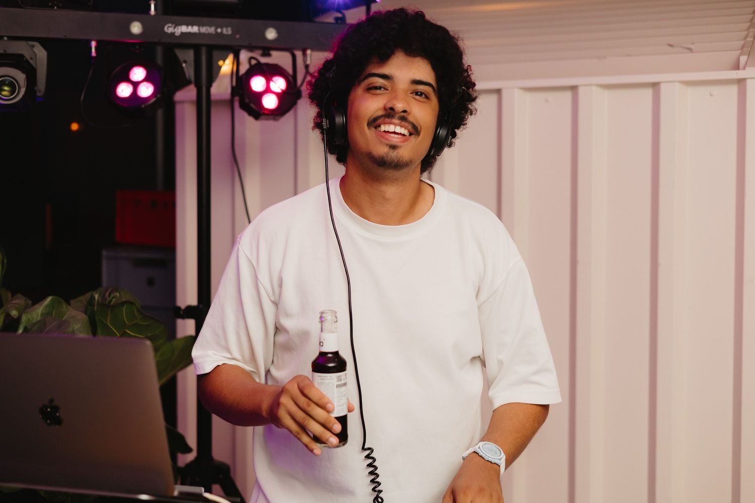 A person in a white t-shirt smiles while holding a mobile device in a well-lit indoor setting.