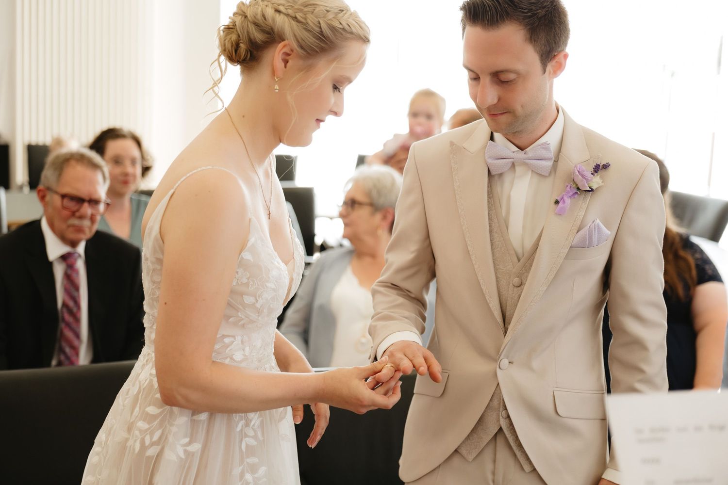 Wedding couple in beige and white attire share a joyful moment during their first dance at an indoor reception.
