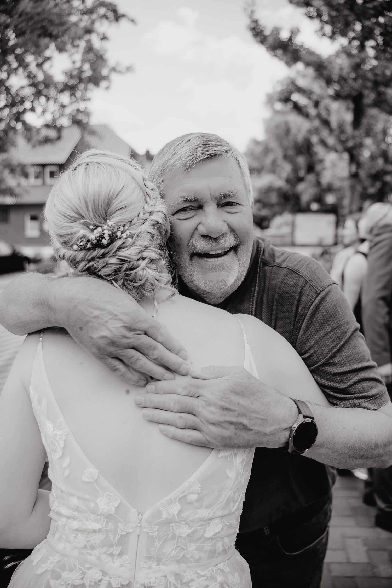 A heartwarming black and white photo showing an emotional embrace at a wedding celebration outdoors.