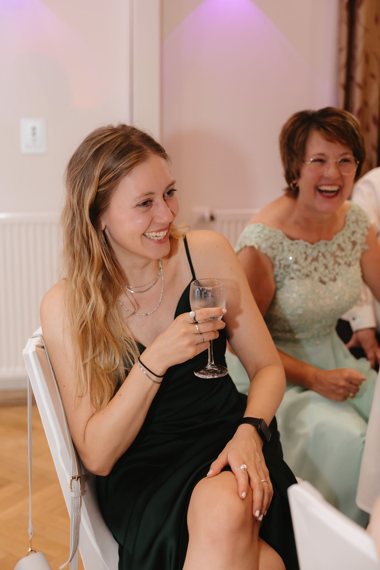 Wedding guests in black and mint green dresses share laughter and drinks at a celebration.