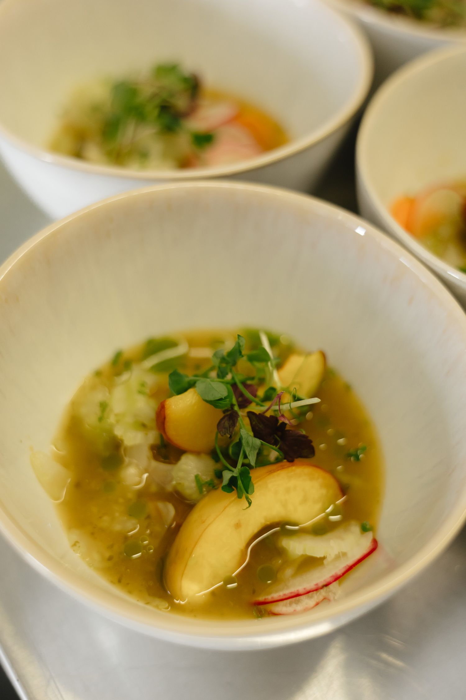 Clear broth soup with potatoes, radish slices and fresh herbs served in a white ceramic bowl.