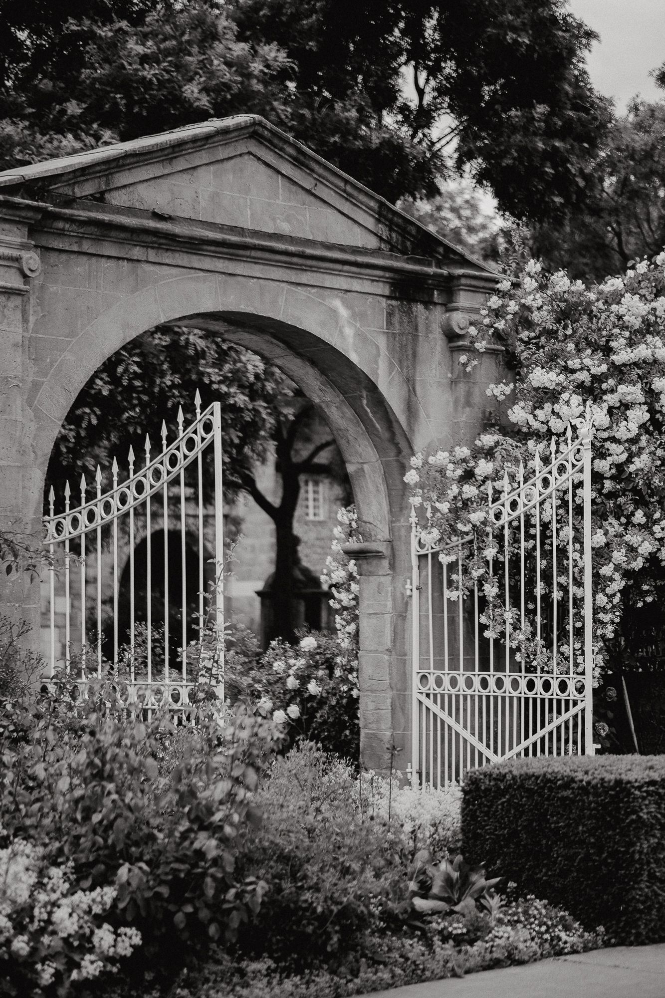 Elegant white iron gates with stone archways in a formal garden setting.