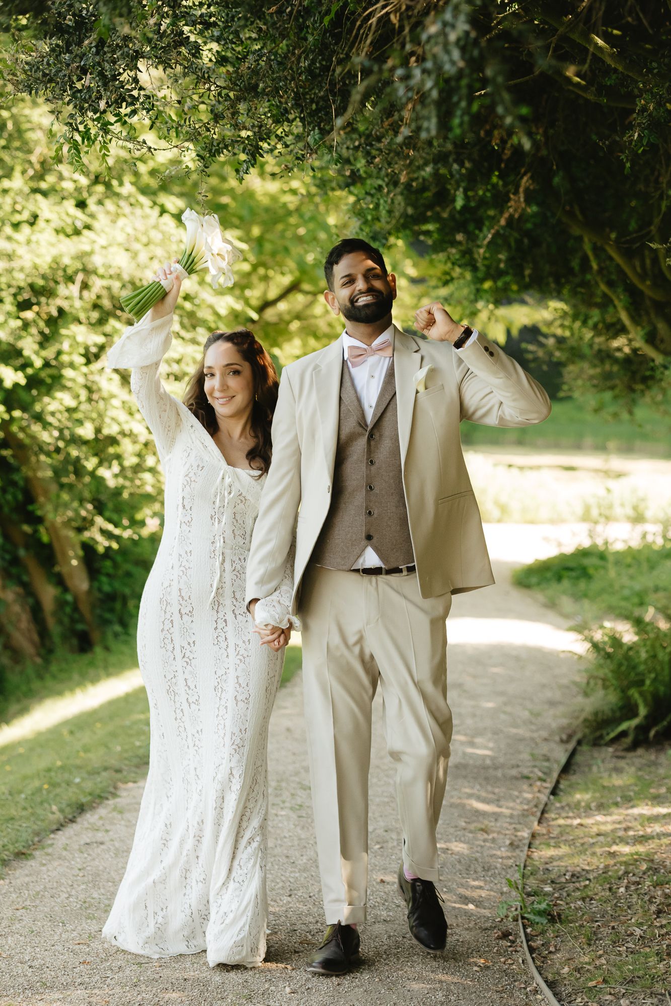Wedding couple walking and laughing together on a garden path in coordinated ivory outfits.