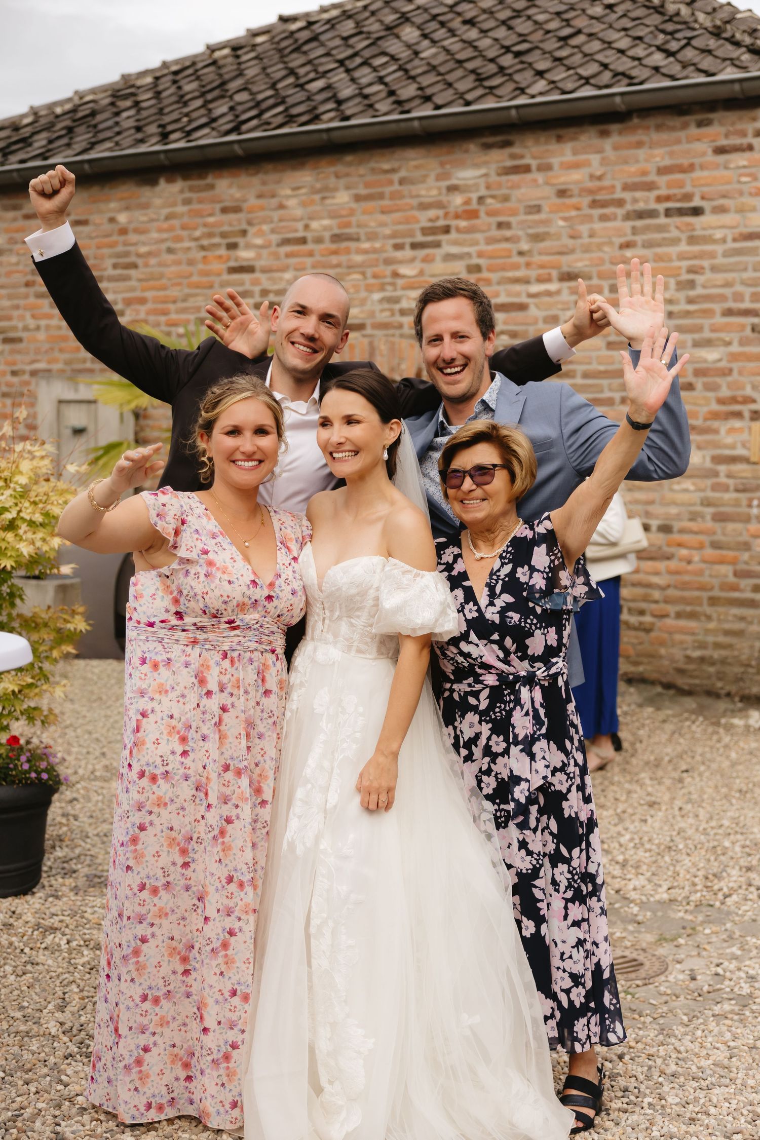 Joyful wedding celebration with guests in floral dresses outside brick venue.