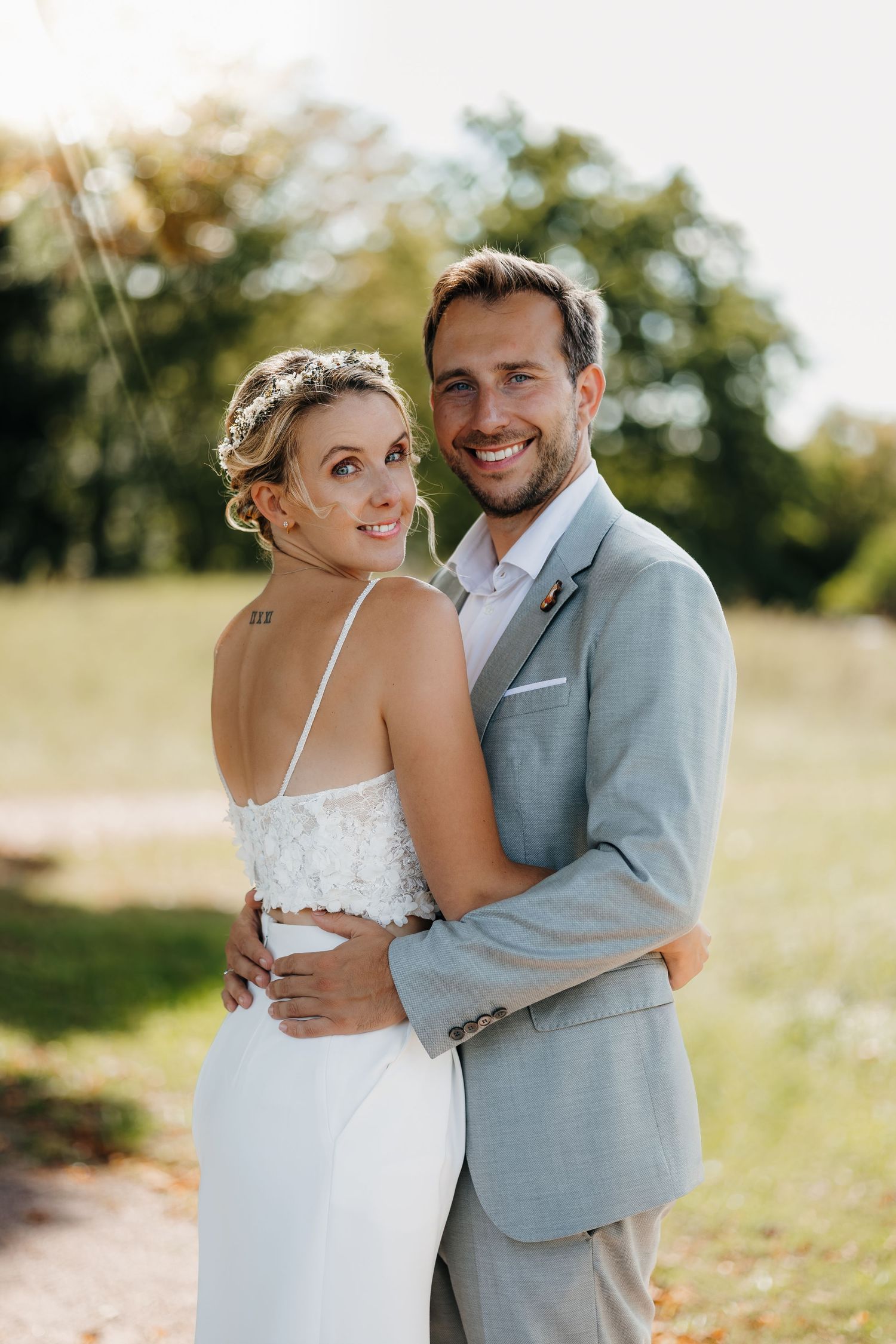 Couple shares an intimate embrace outdoors on their wedding day wearing white dress and light gray suit.