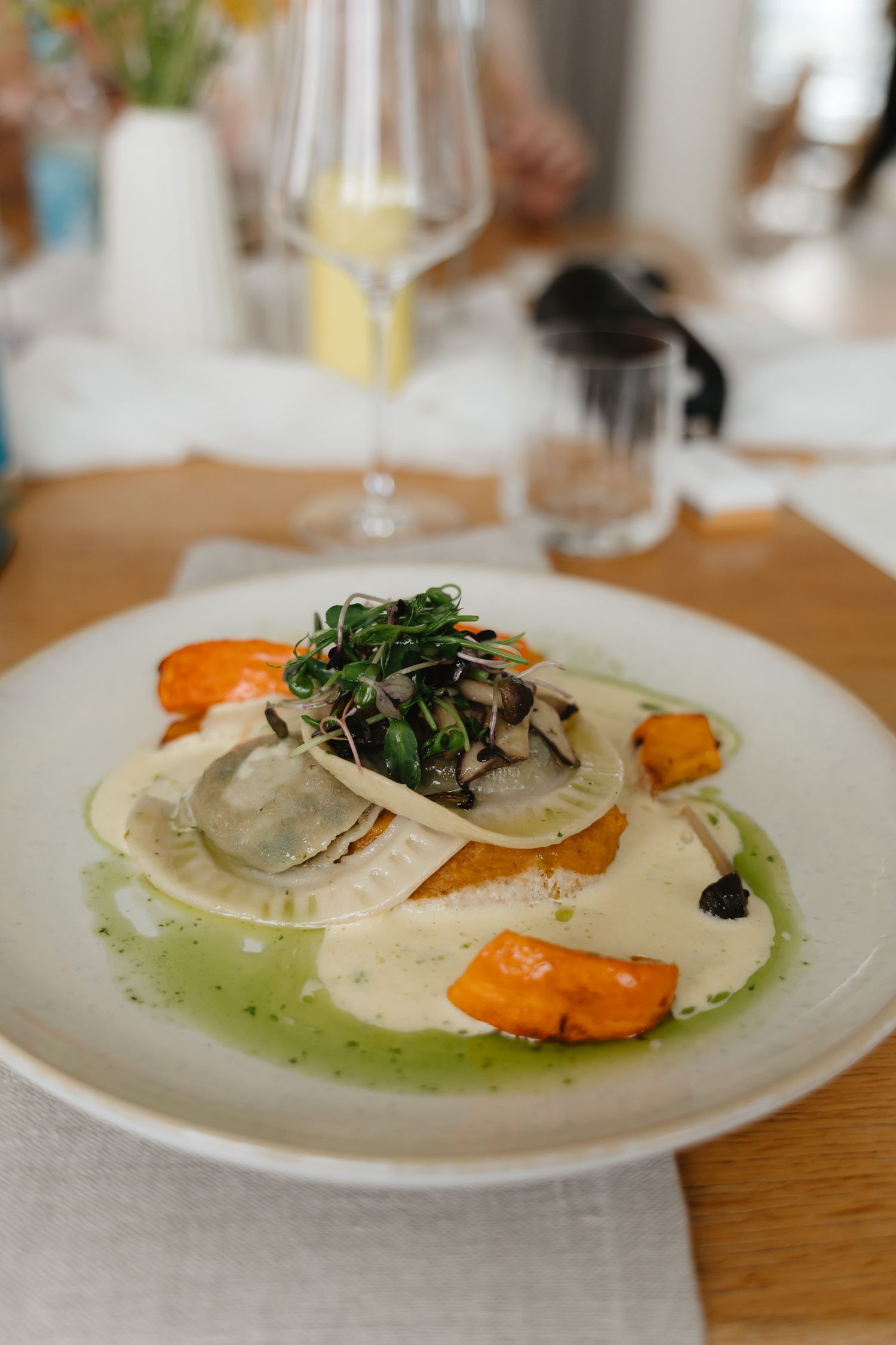 Elegant plated dish featuring thinly sliced mushrooms and greens atop a creamy white sauce with orange garnish.