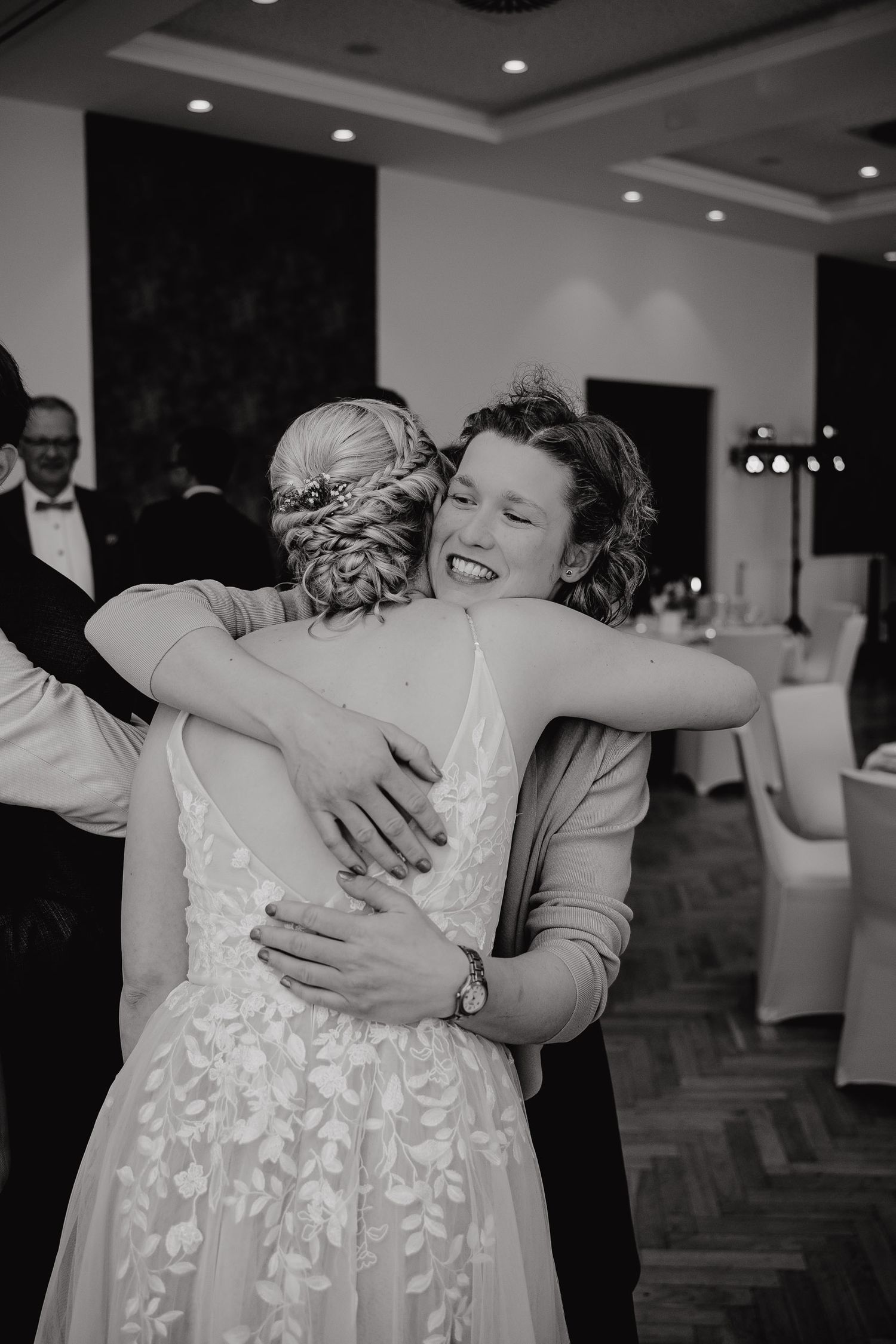 Black and white photo series showing emotional embraces between wedding guests during a reception in an elegant venue.