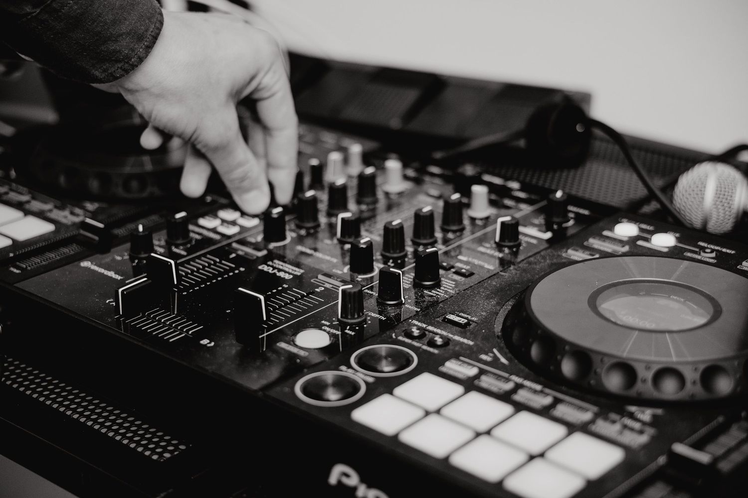 DJ mixer controller with hands adjusting knobs and faders in black and white photography.
