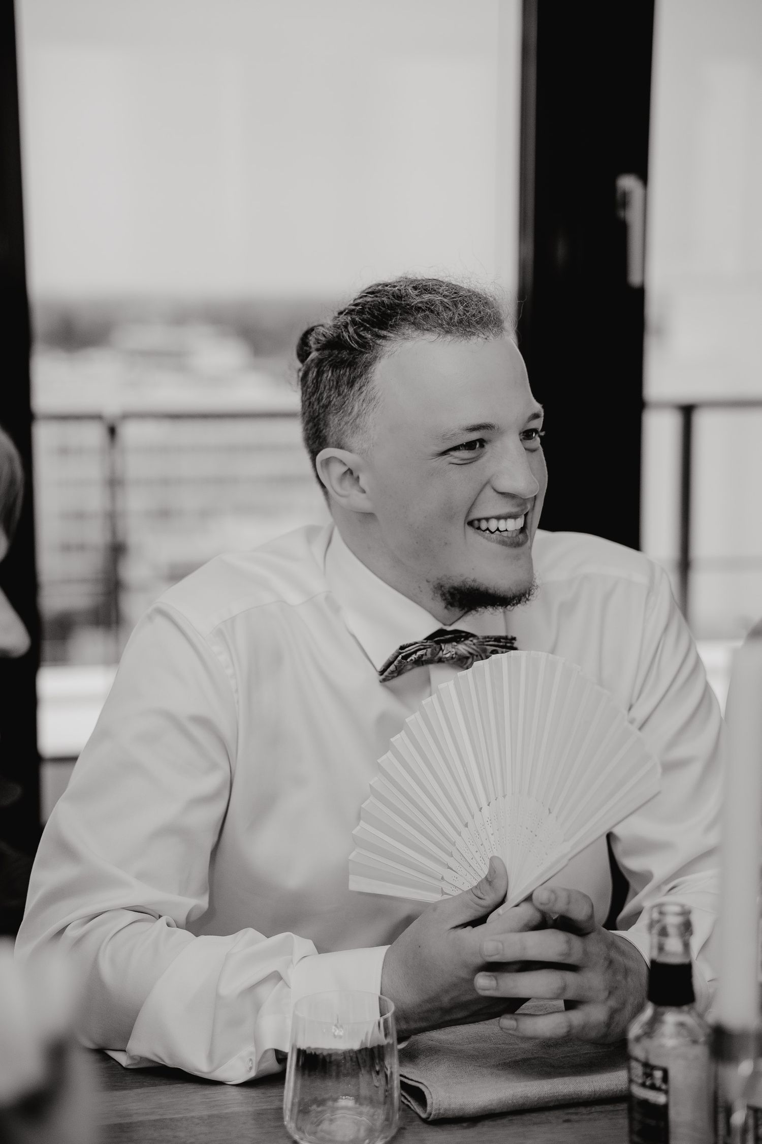A sequence of black and white photos showing a person in white shirt laughing while holding a paper fan.