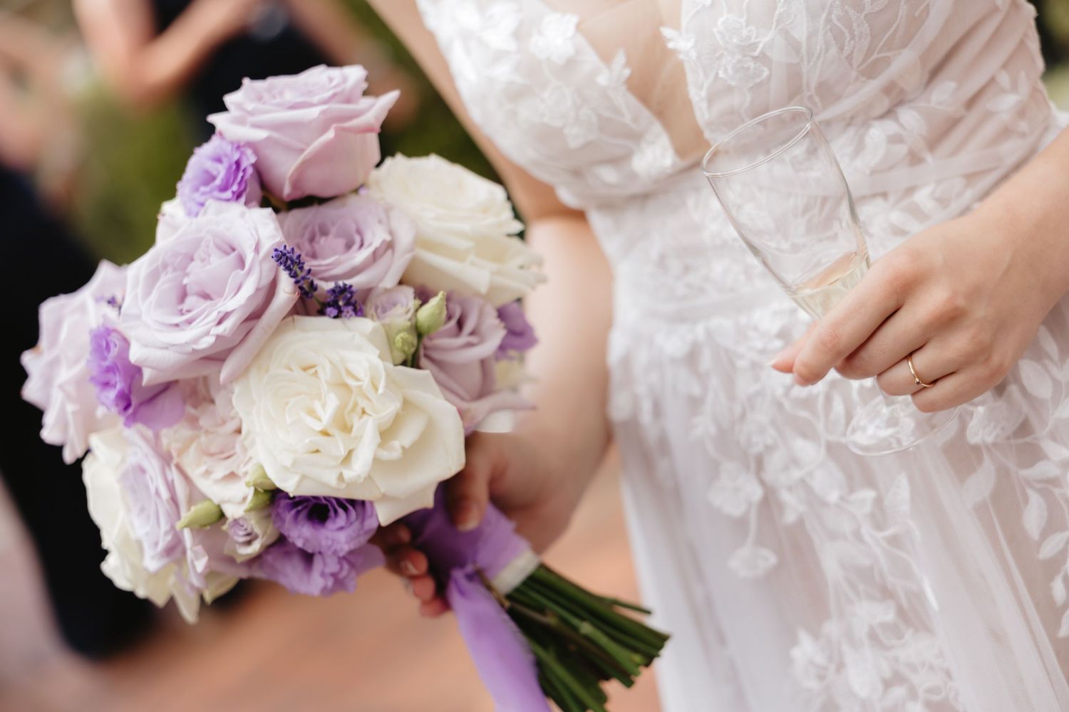 Wedding bouquet with purple and white lisianthus flowers held against a white lace dress in romantic setting.