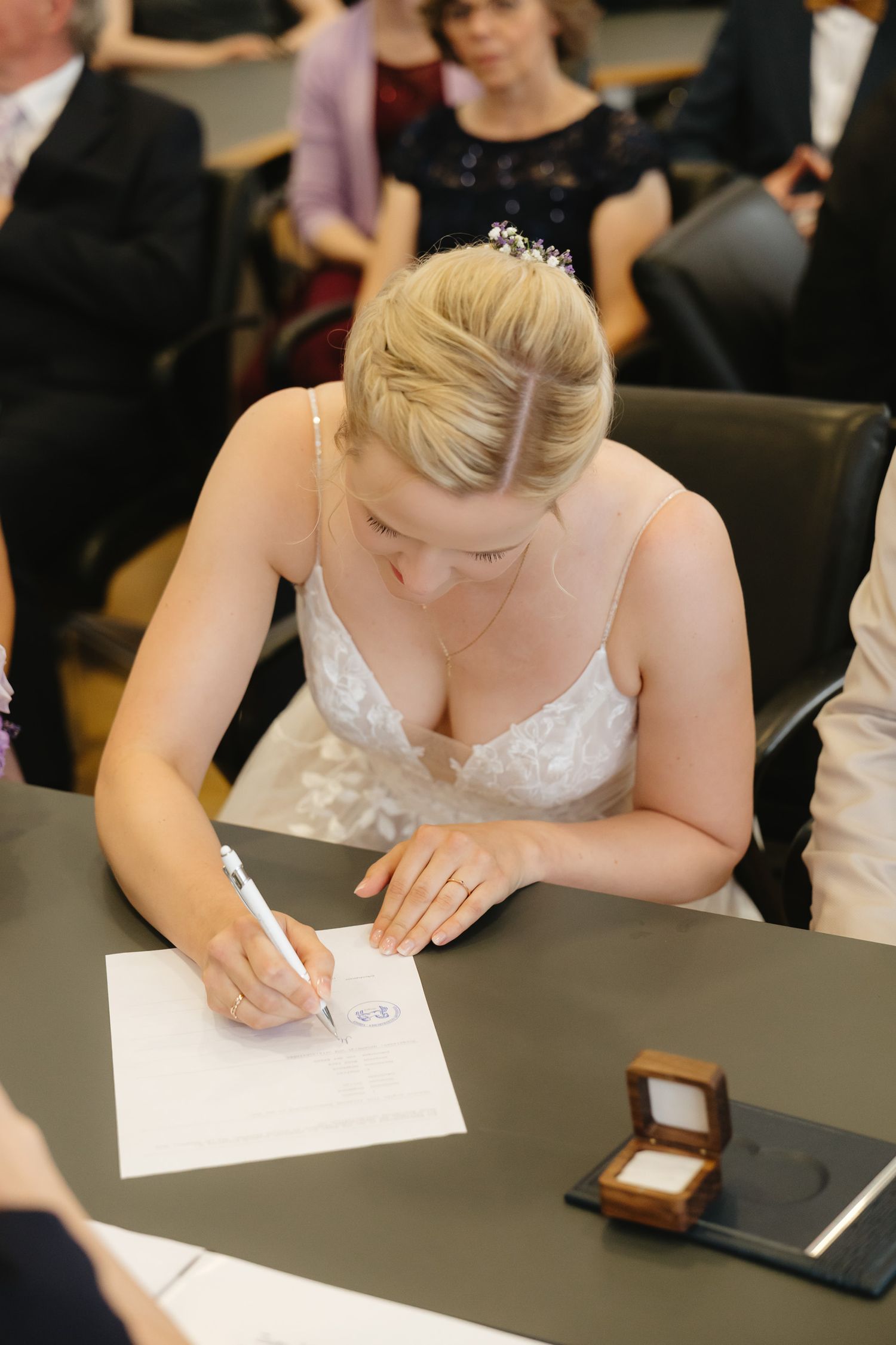 A bride in a white dress signs wedding documents at a table during a civil ceremony.