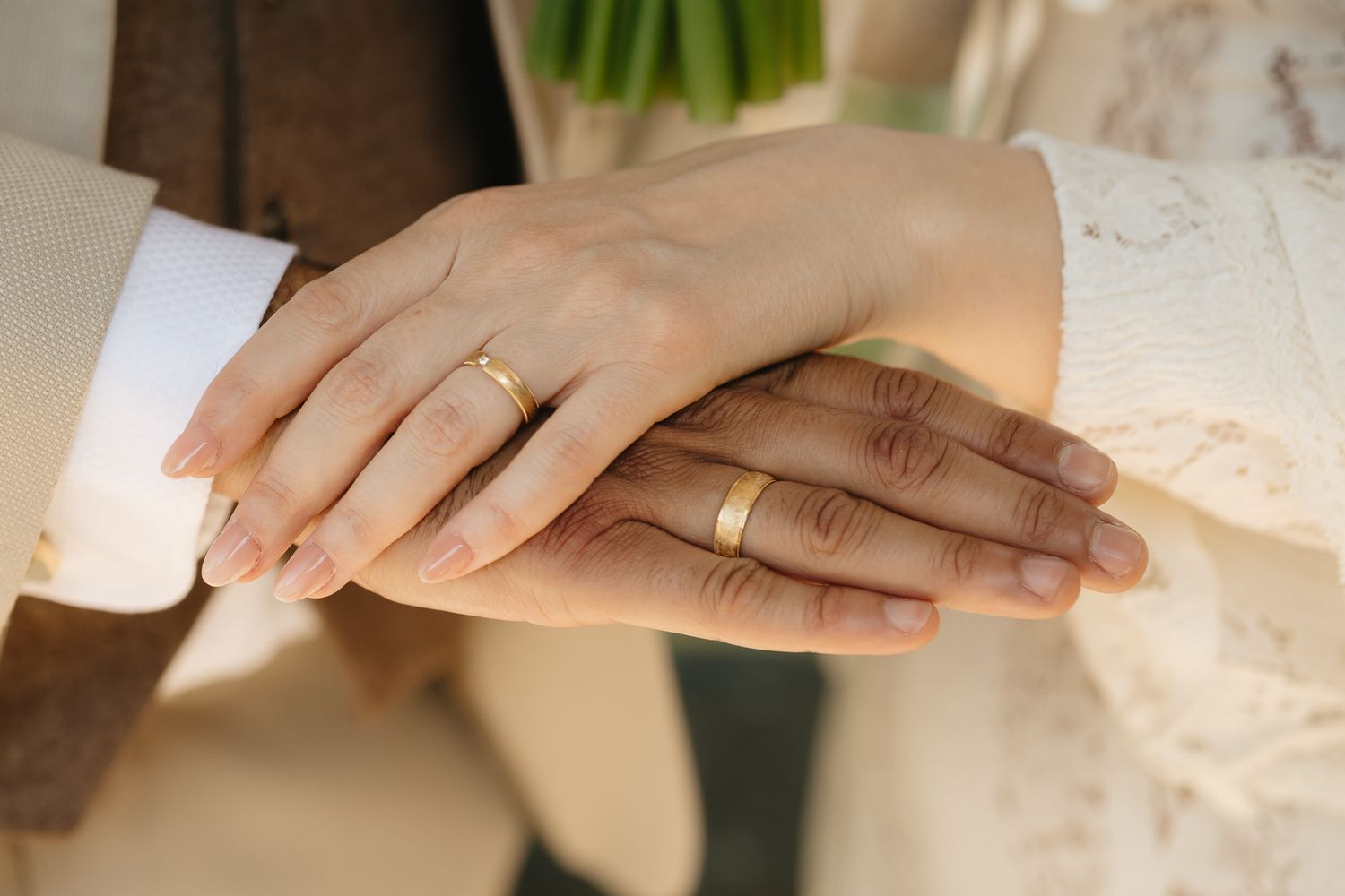 Close-up details of wedding rings and hands against white lace fabric.