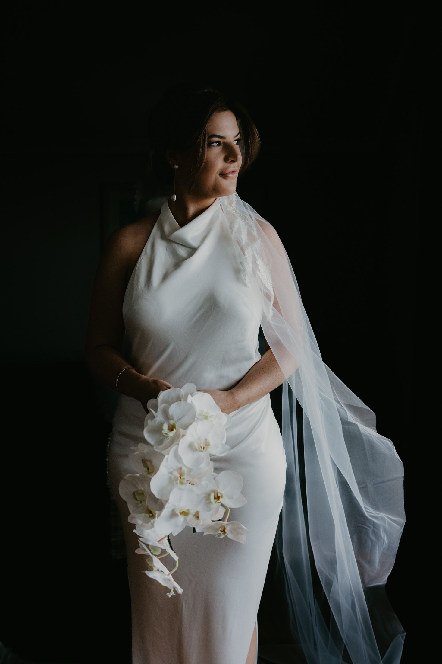 Bride portrait photograph with natural window light highlighting her against dark background